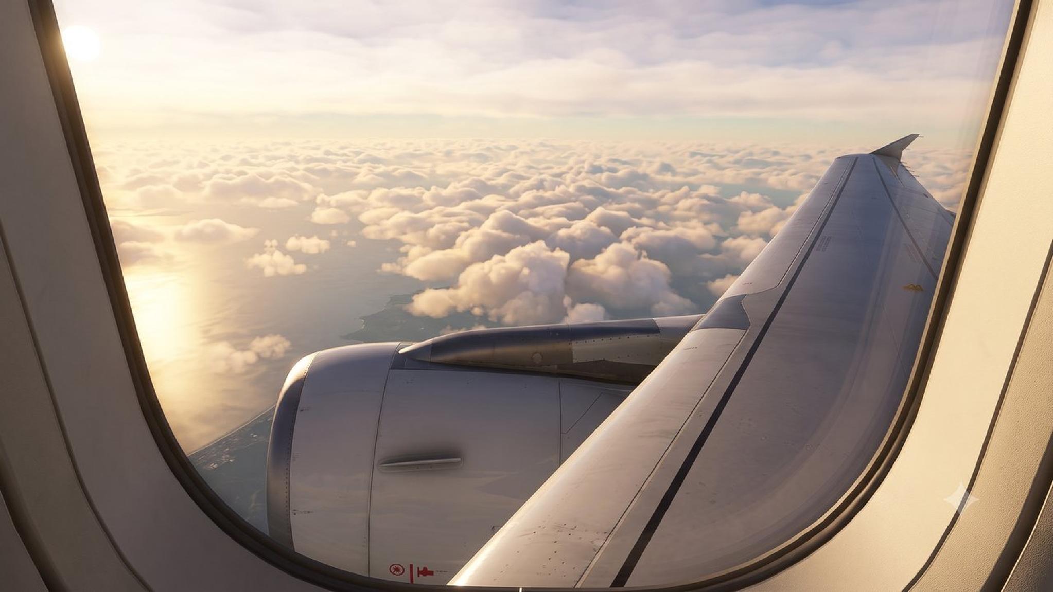 Airplane wing and engine above sunlit clouds and ocean from window. Travel.
