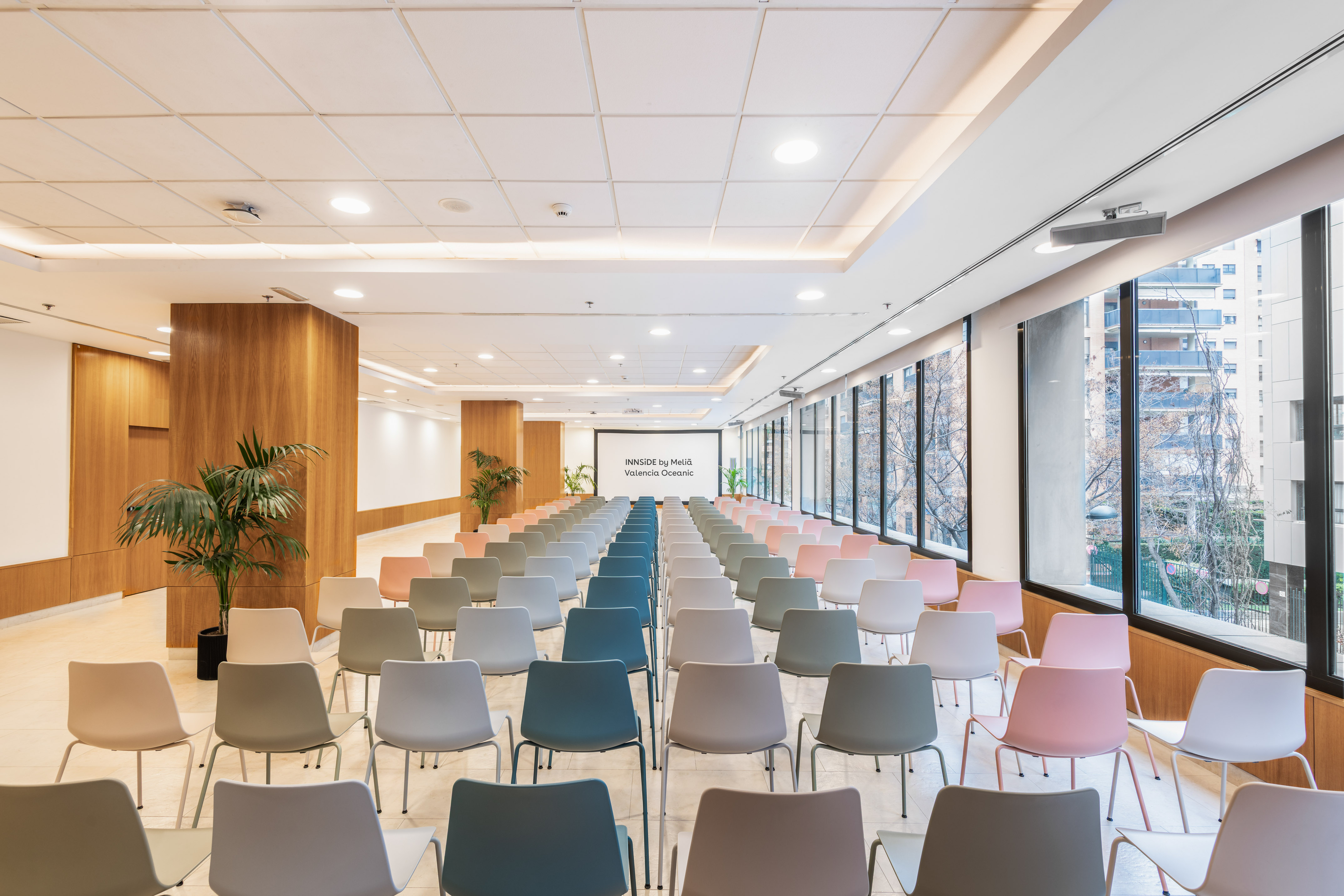 Modern conference room at INNSiDE Valencia Oceanic with colored chairs and screen.
