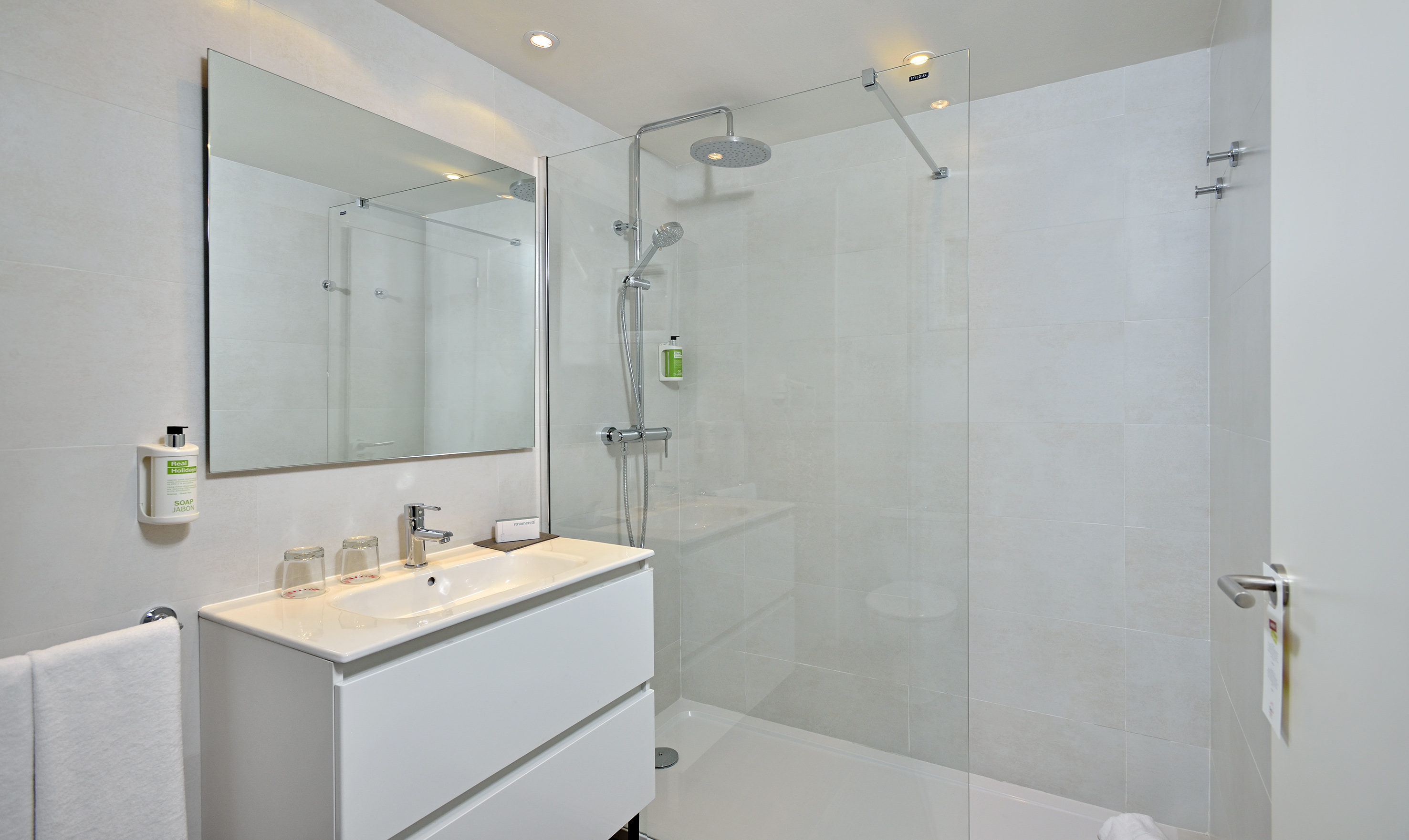 Modern hotel bathroom with walk-in glass shower, vanity, and mirror.