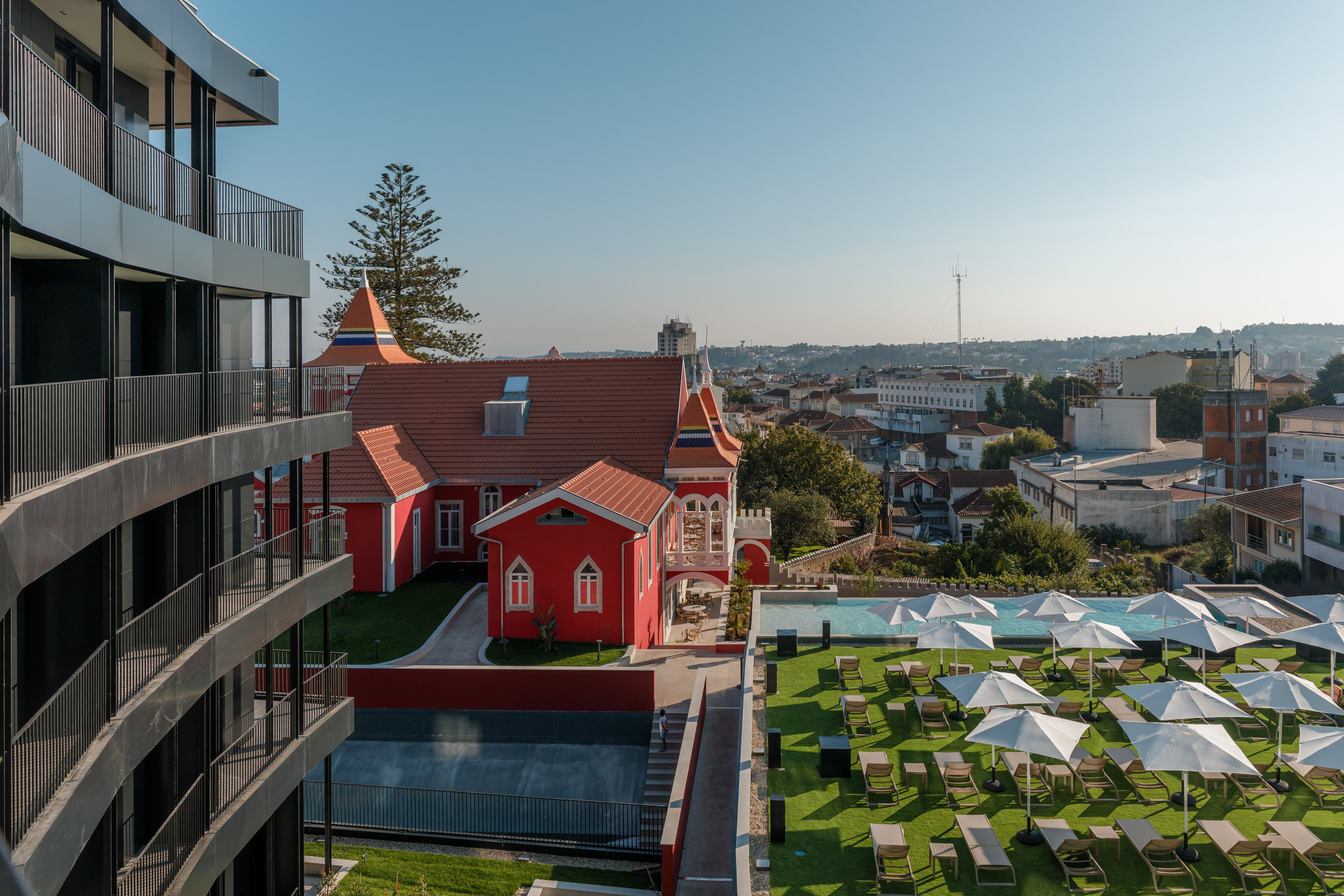 Modern and historic hotel buildings, outdoor pool with sun loungers, city backdrop.