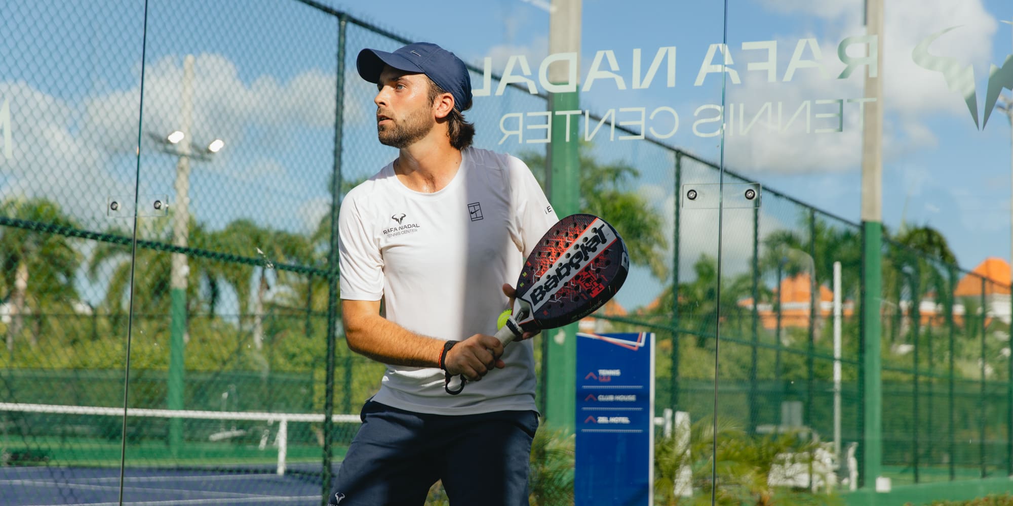 Padel player in cap holding Babolat racket at Rafa Nadal Tennis Center.