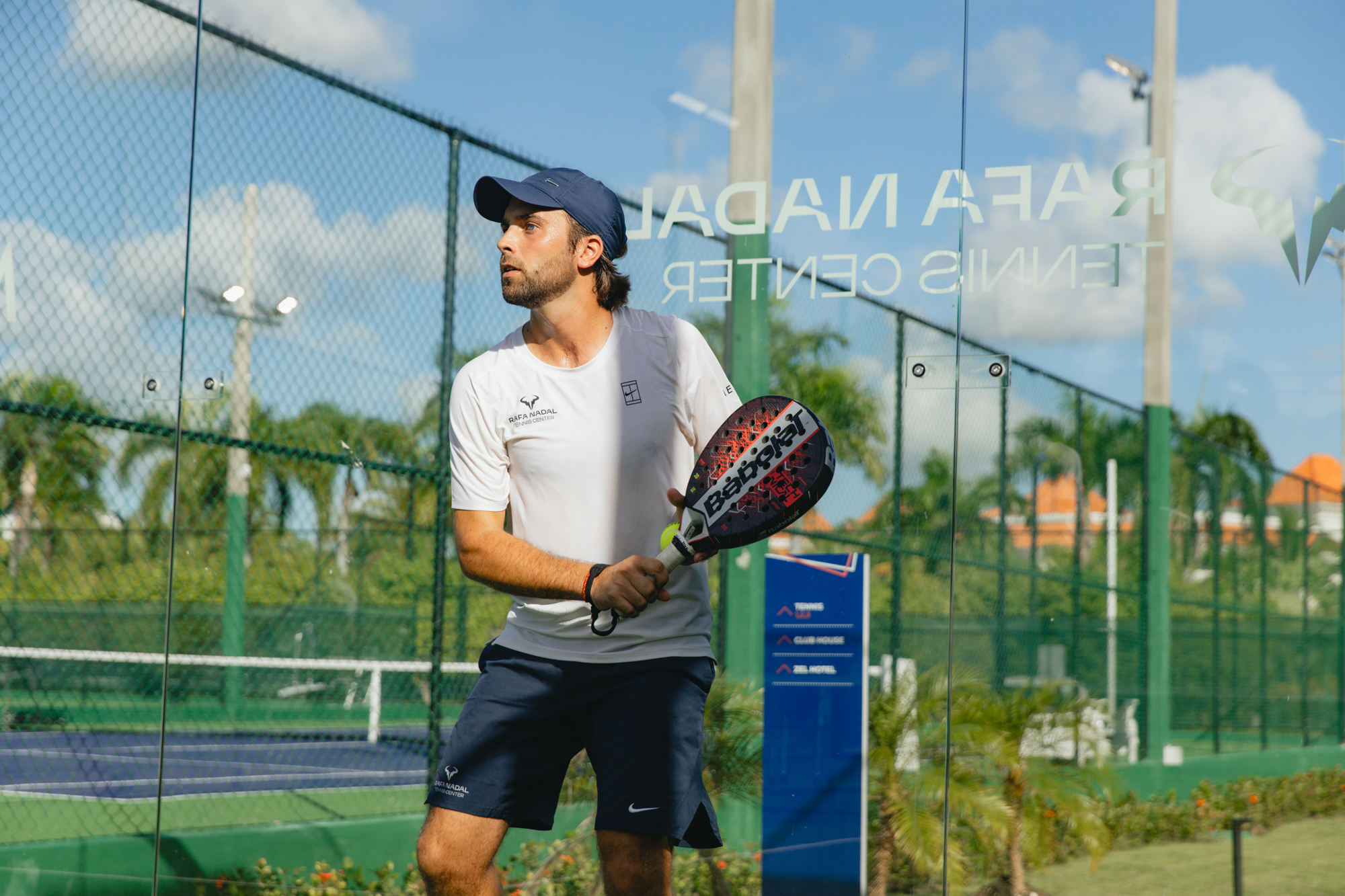 Padel player in cap holding Babolat racket at Rafa Nadal Tennis Center.