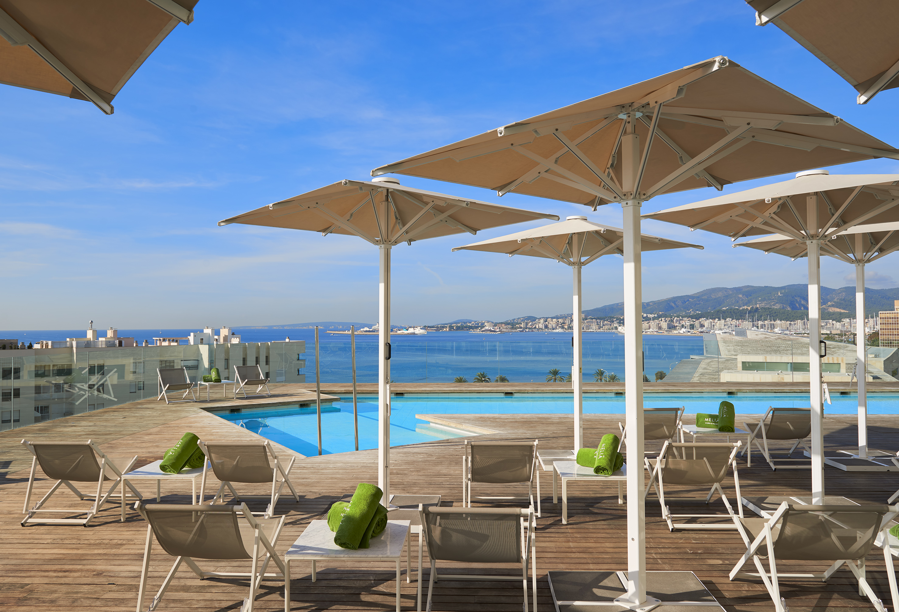 Rooftop pool deck with lounge chairs, umbrellas, ocean and city views.