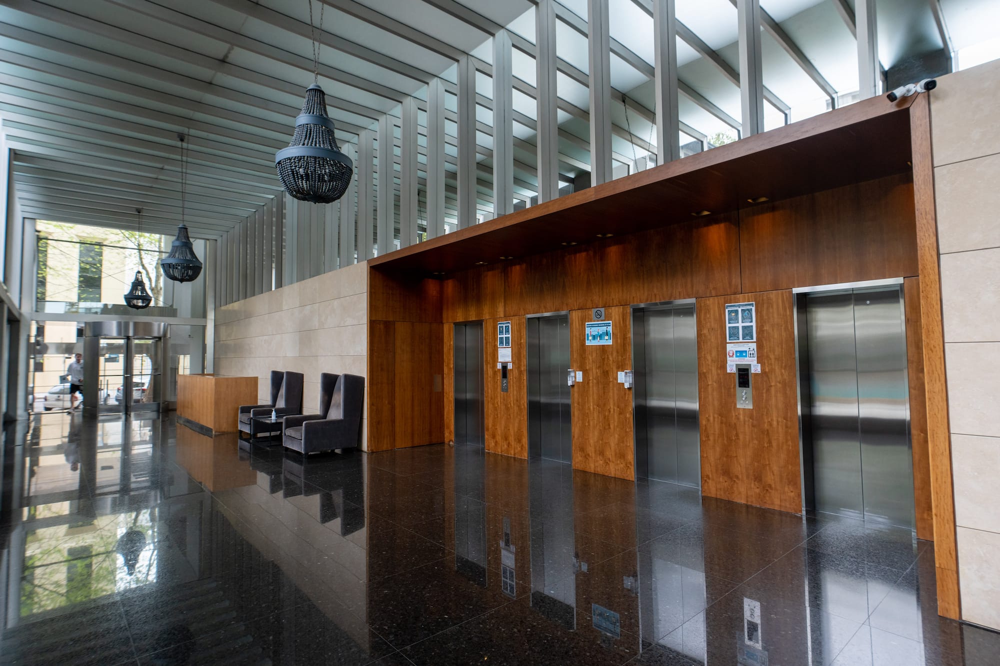 Modern building lobby with wood elevators, reflective black floor, and pendant chandeliers.