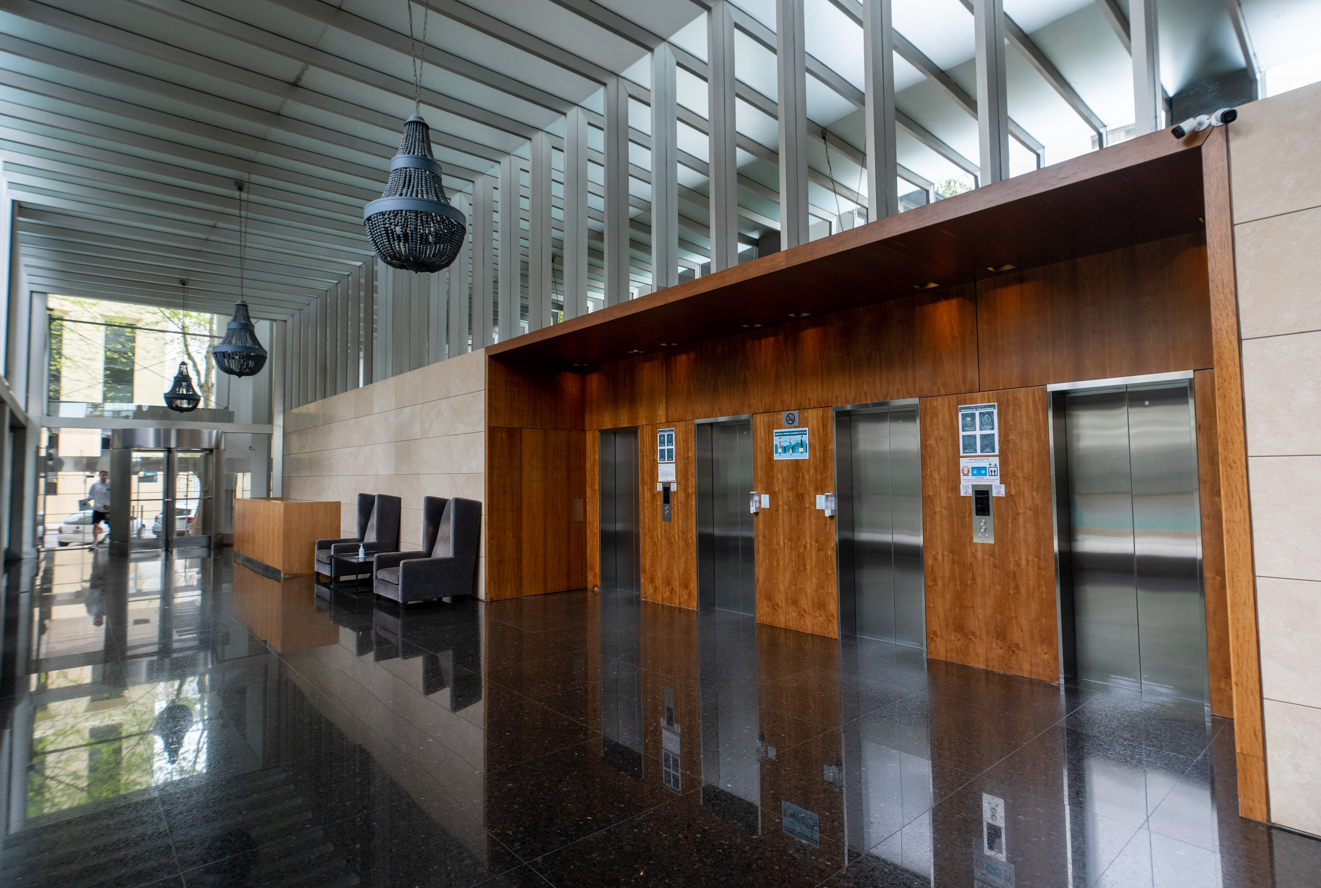 Modern building lobby with wood elevators, reflective black floor, and pendant chandeliers.