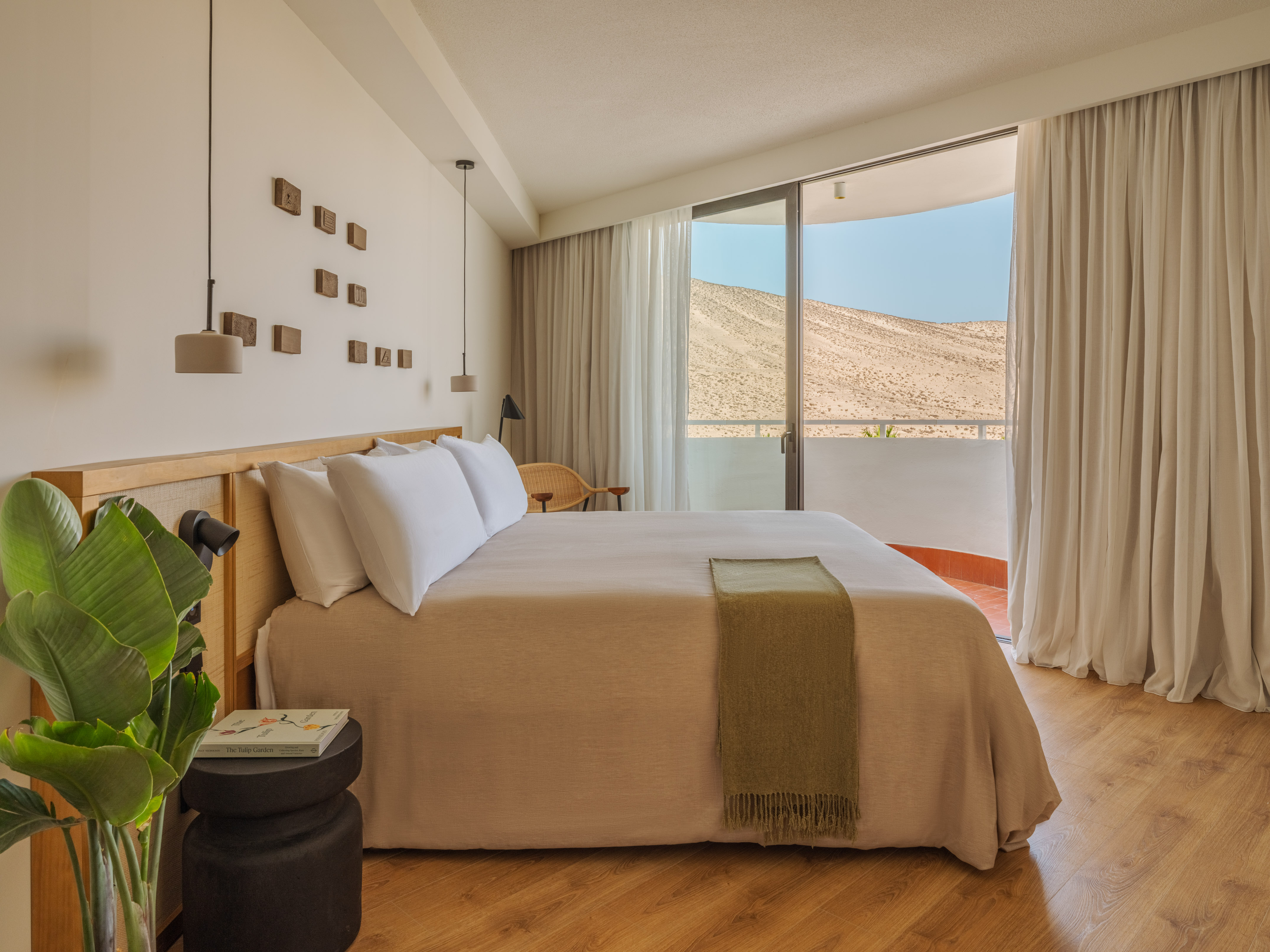 Minimalist hotel bedroom with desert mountain view and natural wood accents.