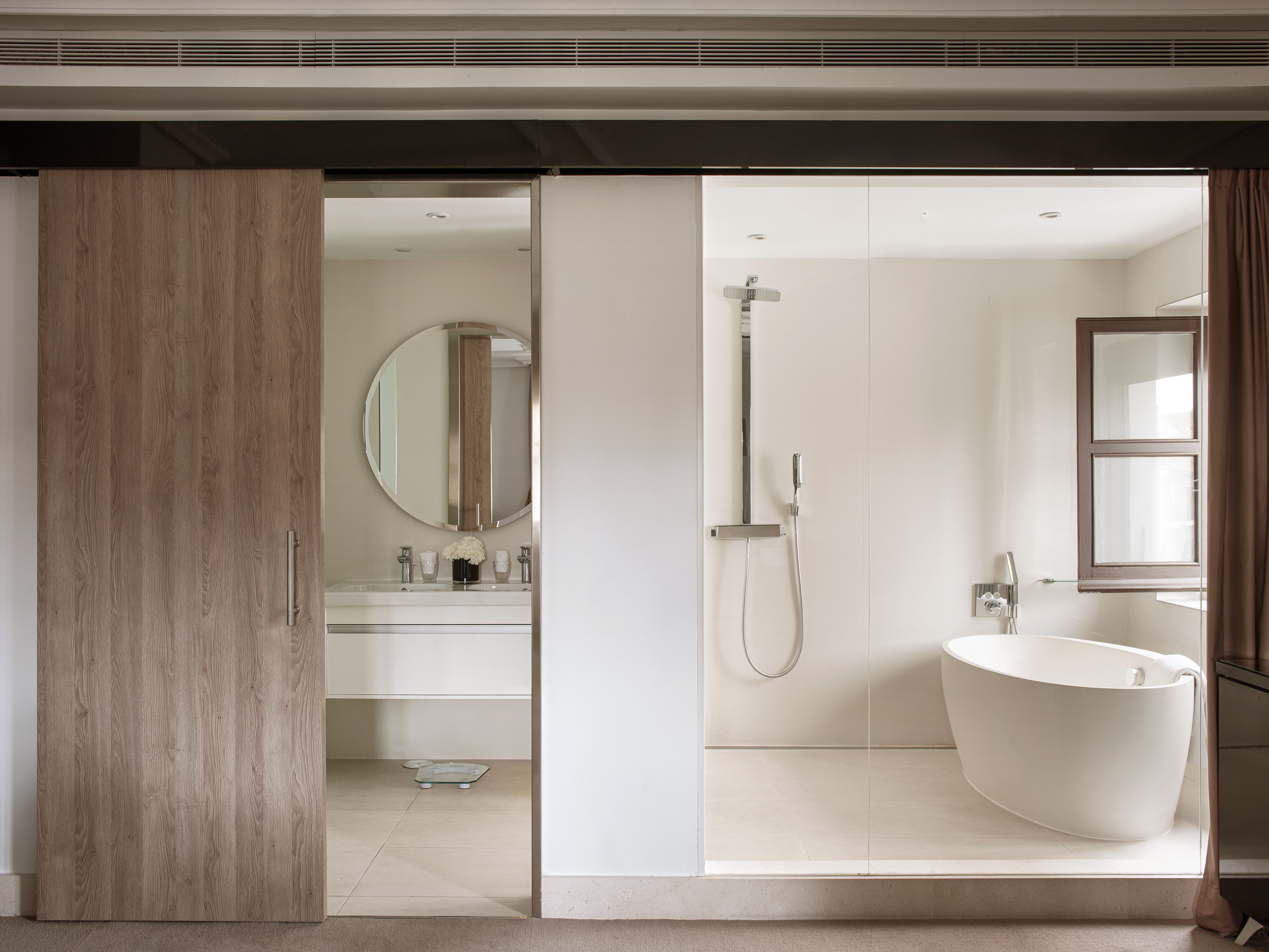 Modern bathroom with sliding door, round mirror, freestanding tub, and glass shower.