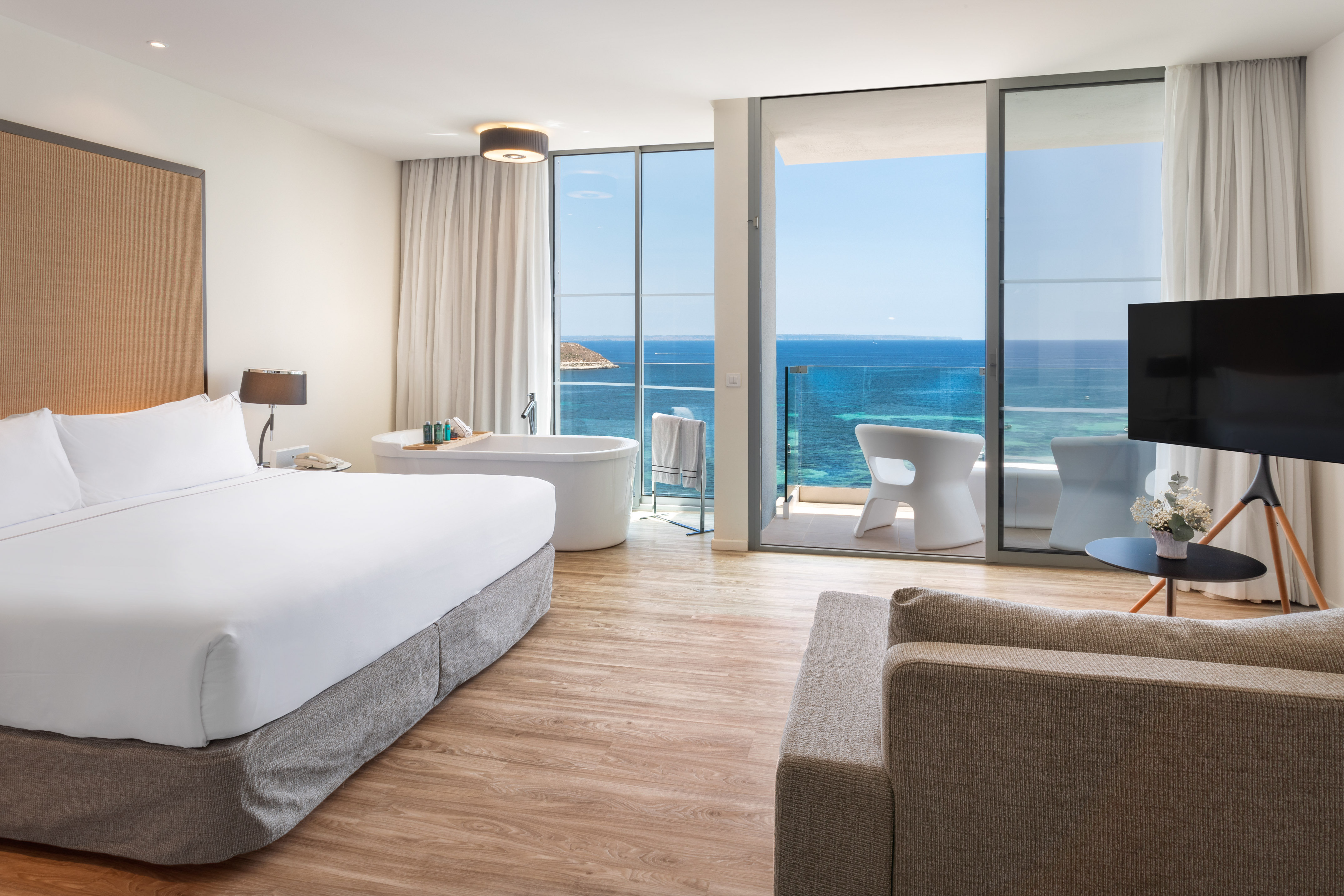 Modern hotel room with king bed, soaker tub, and ocean view balcony.