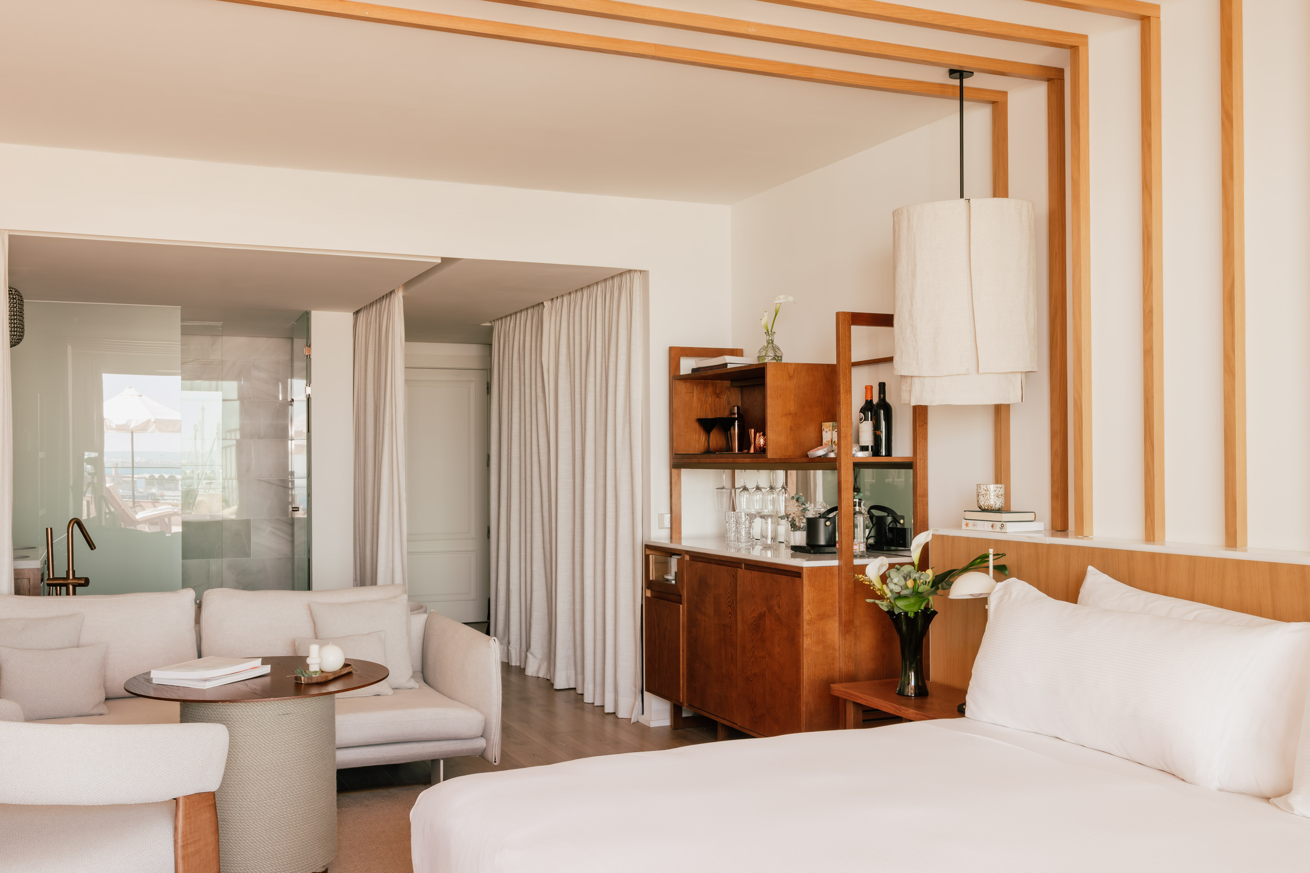 Modern hotel suite with bed, sofa, minibar, and ocean view terrace.