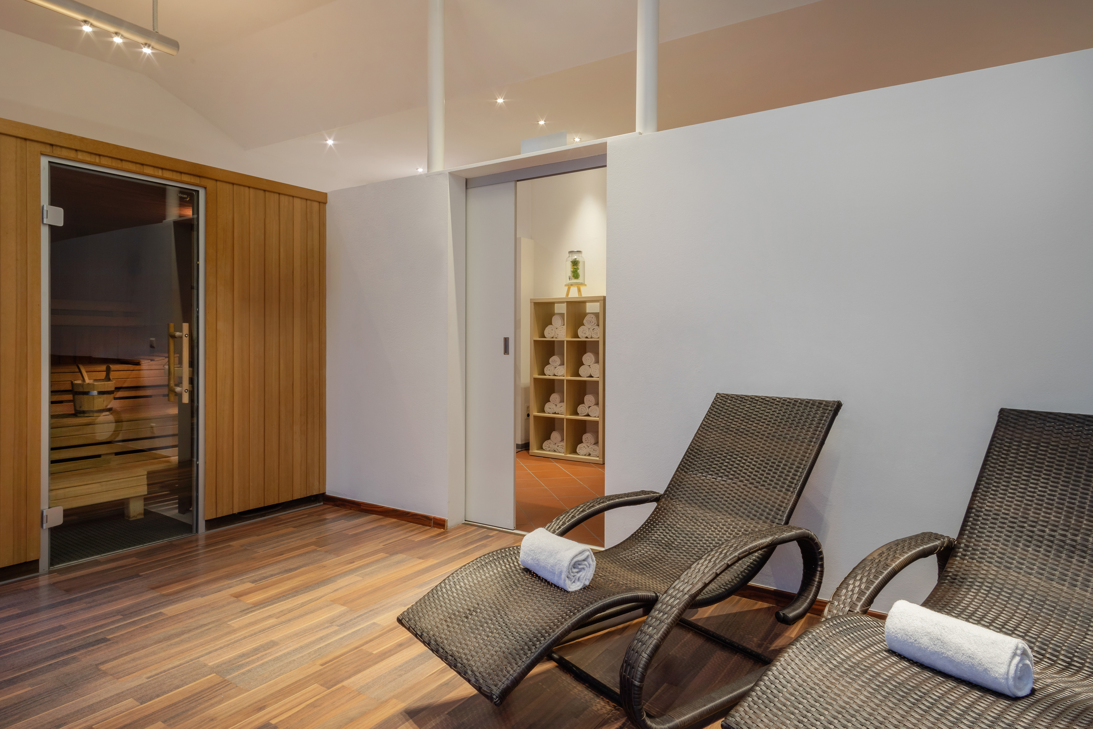 Wellness area with wooden sauna, two lounge chairs, and towel display.