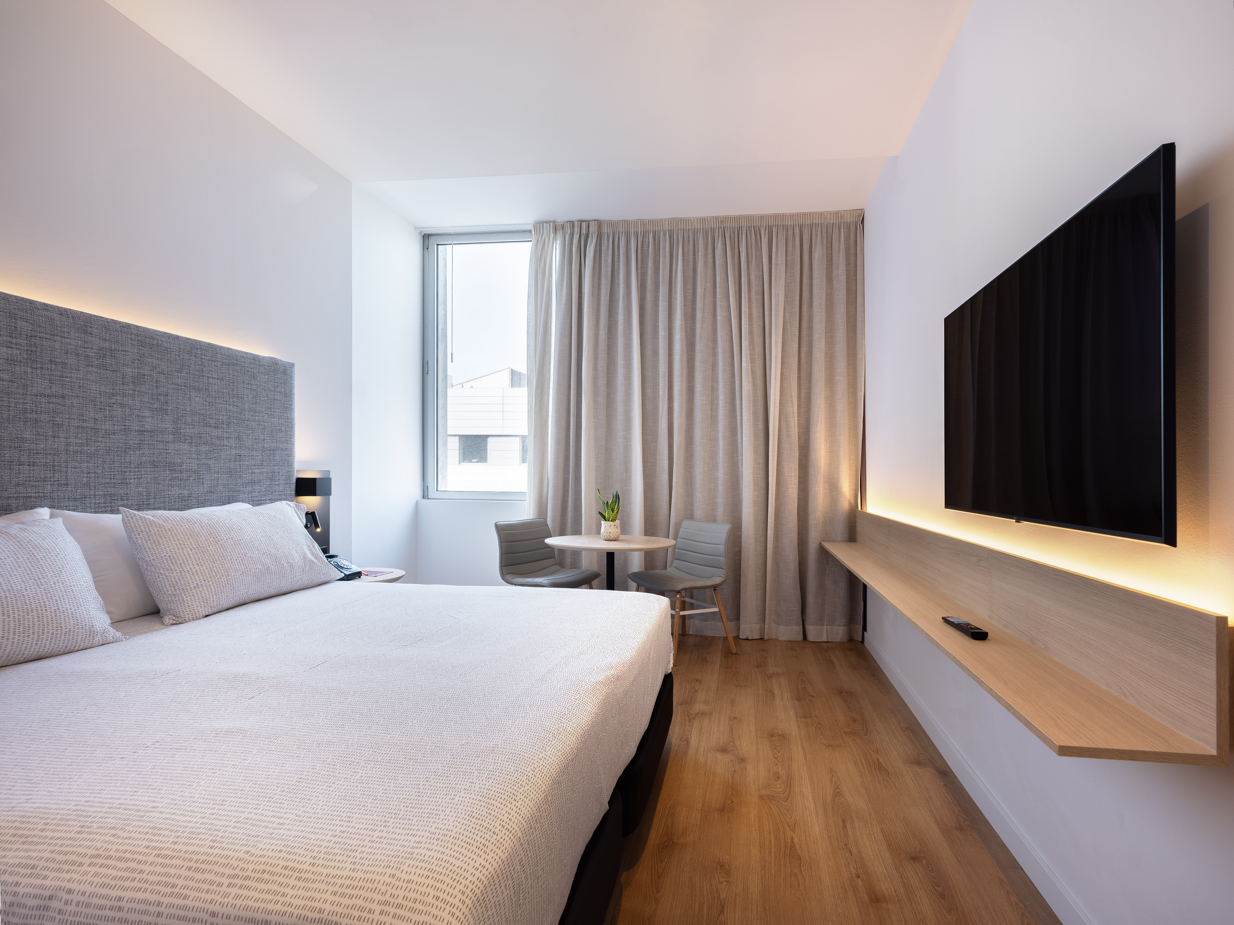 Modern hotel room with king bed, wall TV, seating area, and hardwood floor.
