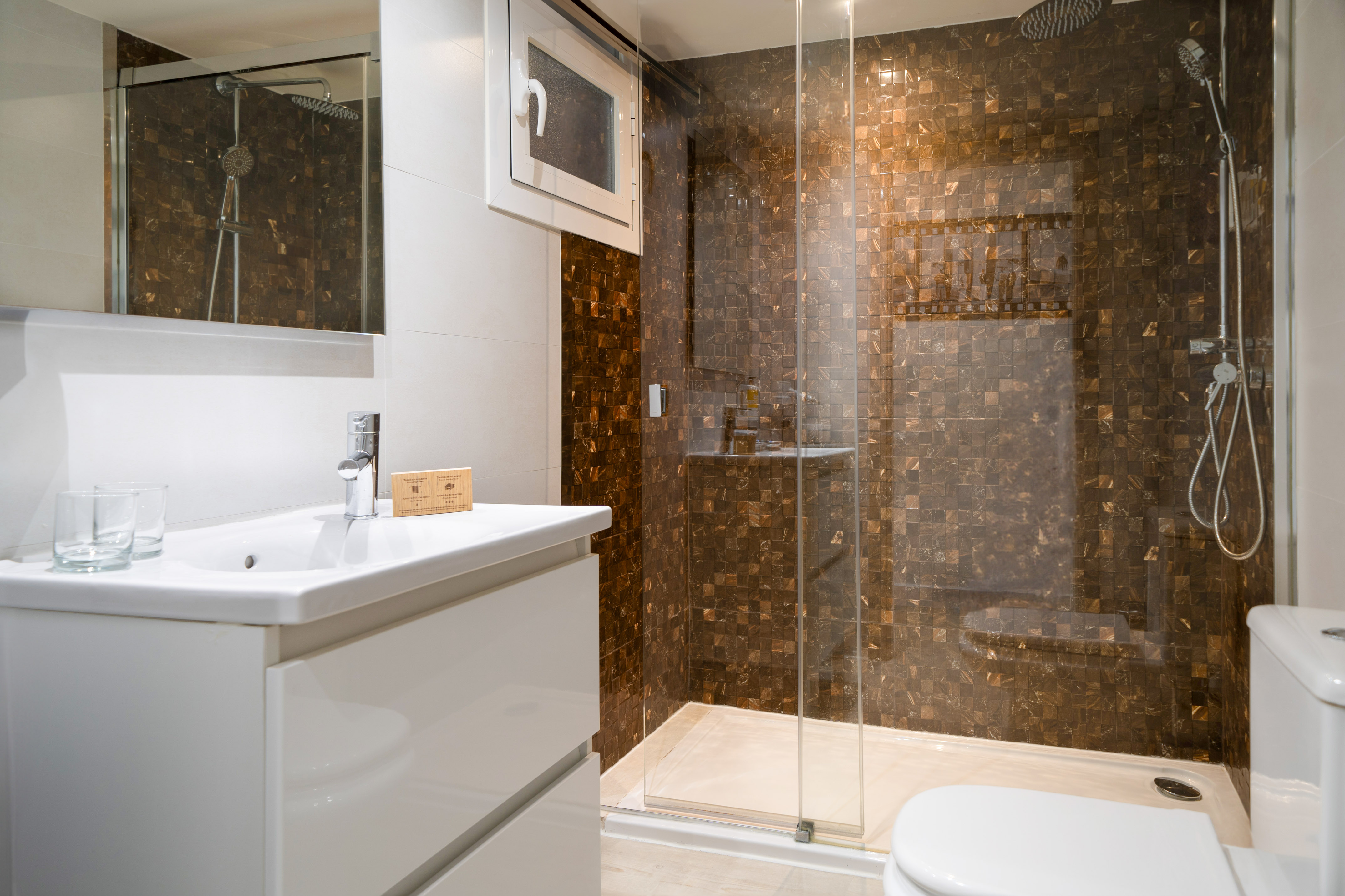 Modern bathroom with white vanity, sink, and brown mosaic tiled shower.
