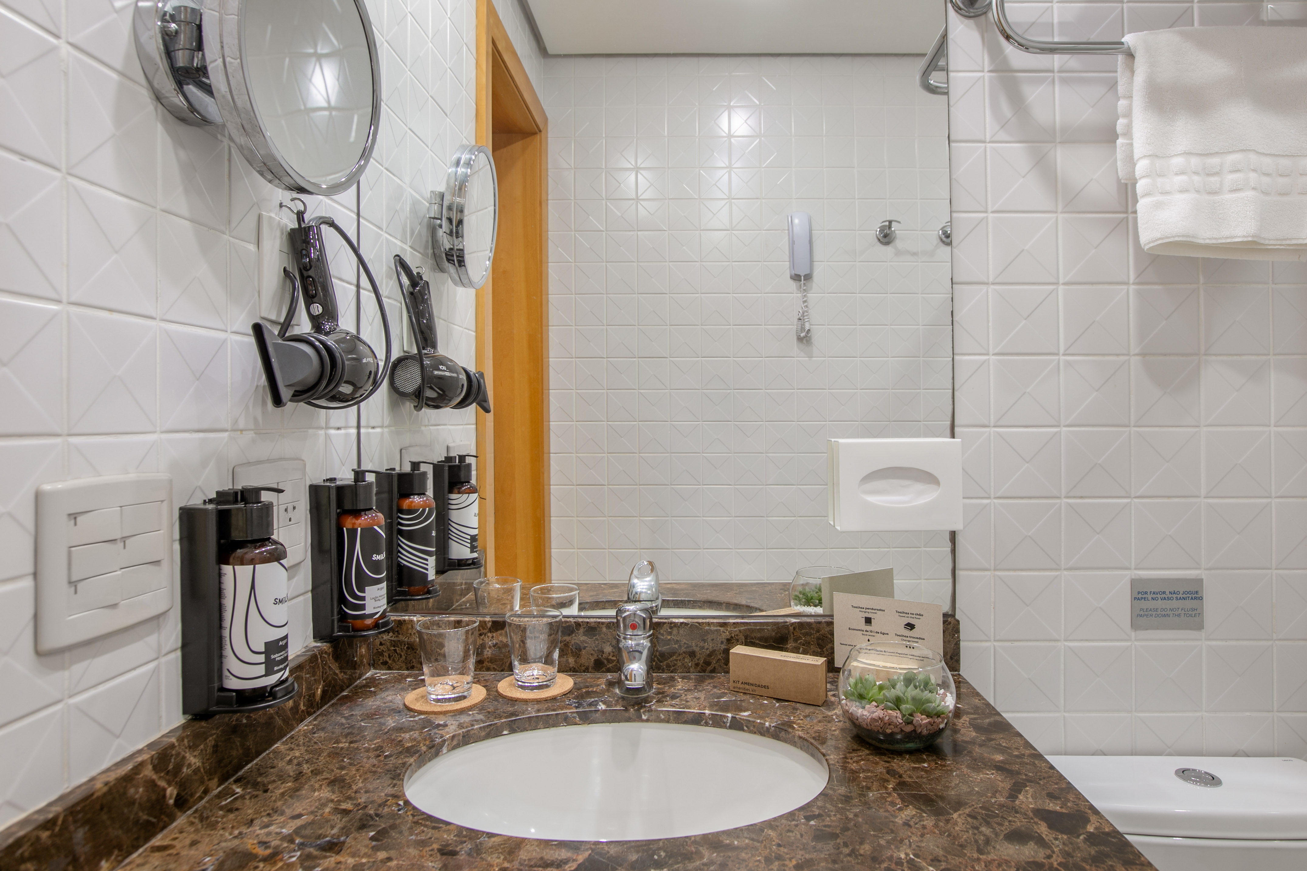 Modern hotel bathroom vanity with marble counter, sink, hair dryers, and amenities.