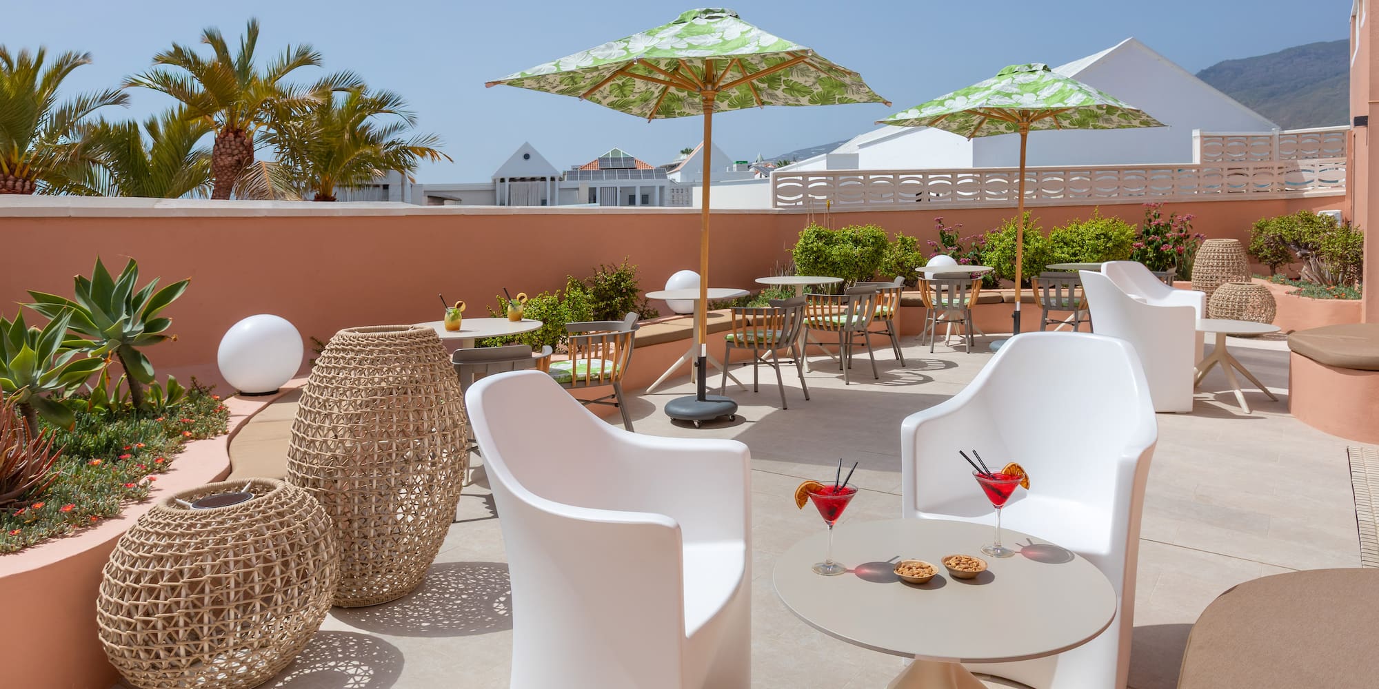 Sunny resort terrace with modern seating, tropical umbrellas, and cocktails.
