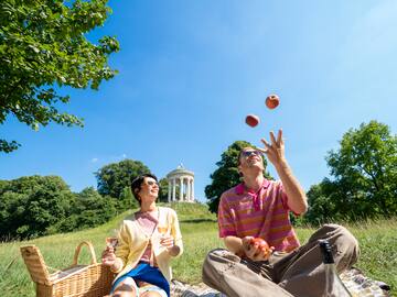 a man and woman sitting on a blanket in a park