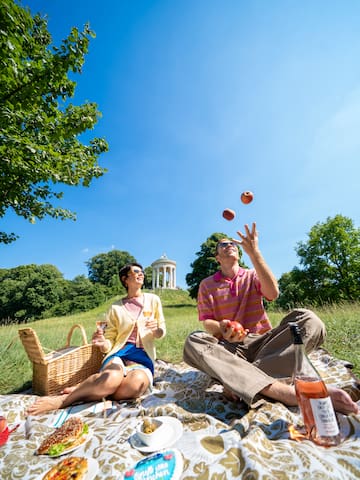 a man and woman sitting on a blanket in a park