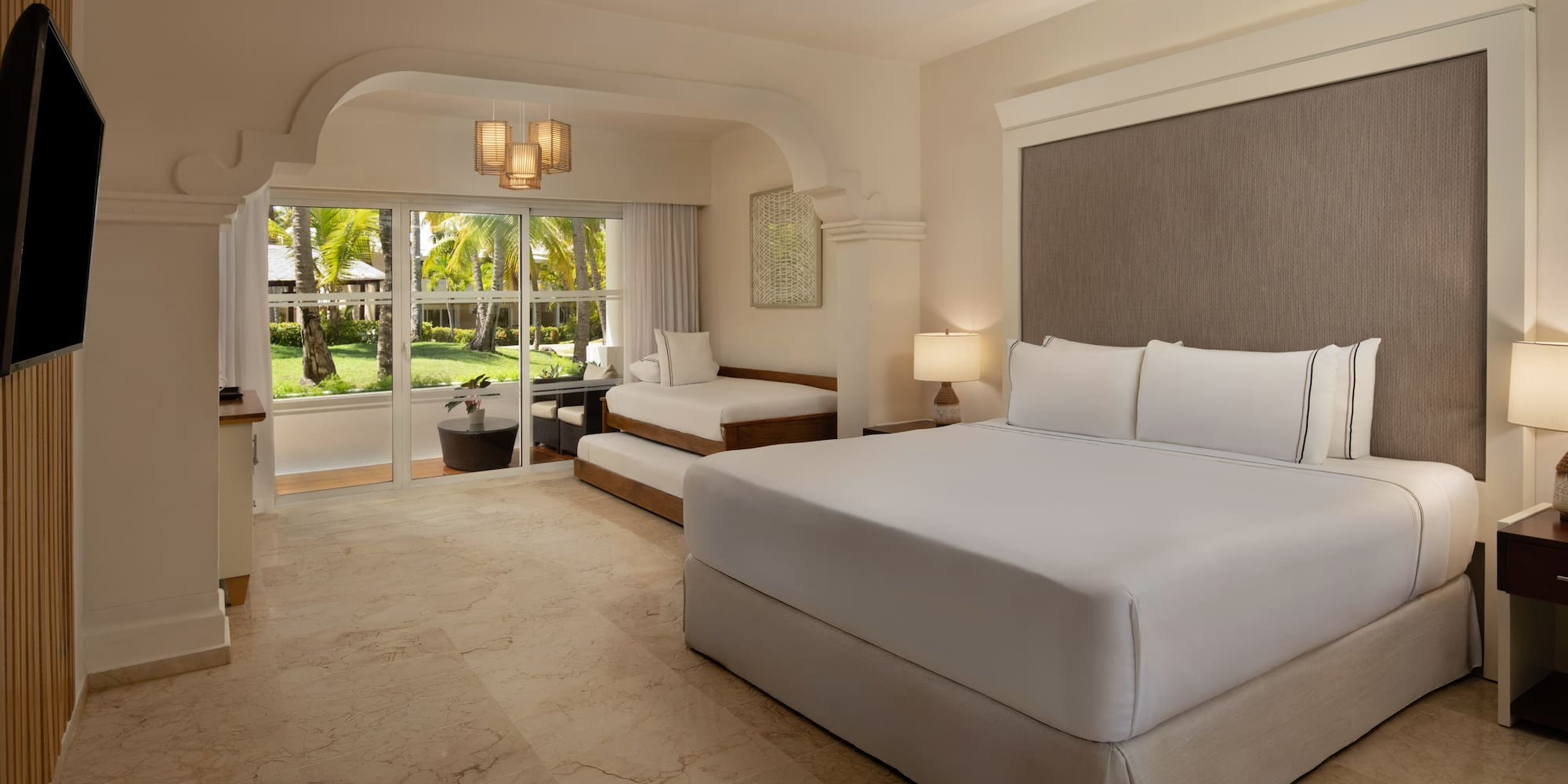 Resort room with king bed, daybed, and lush tropical garden view.