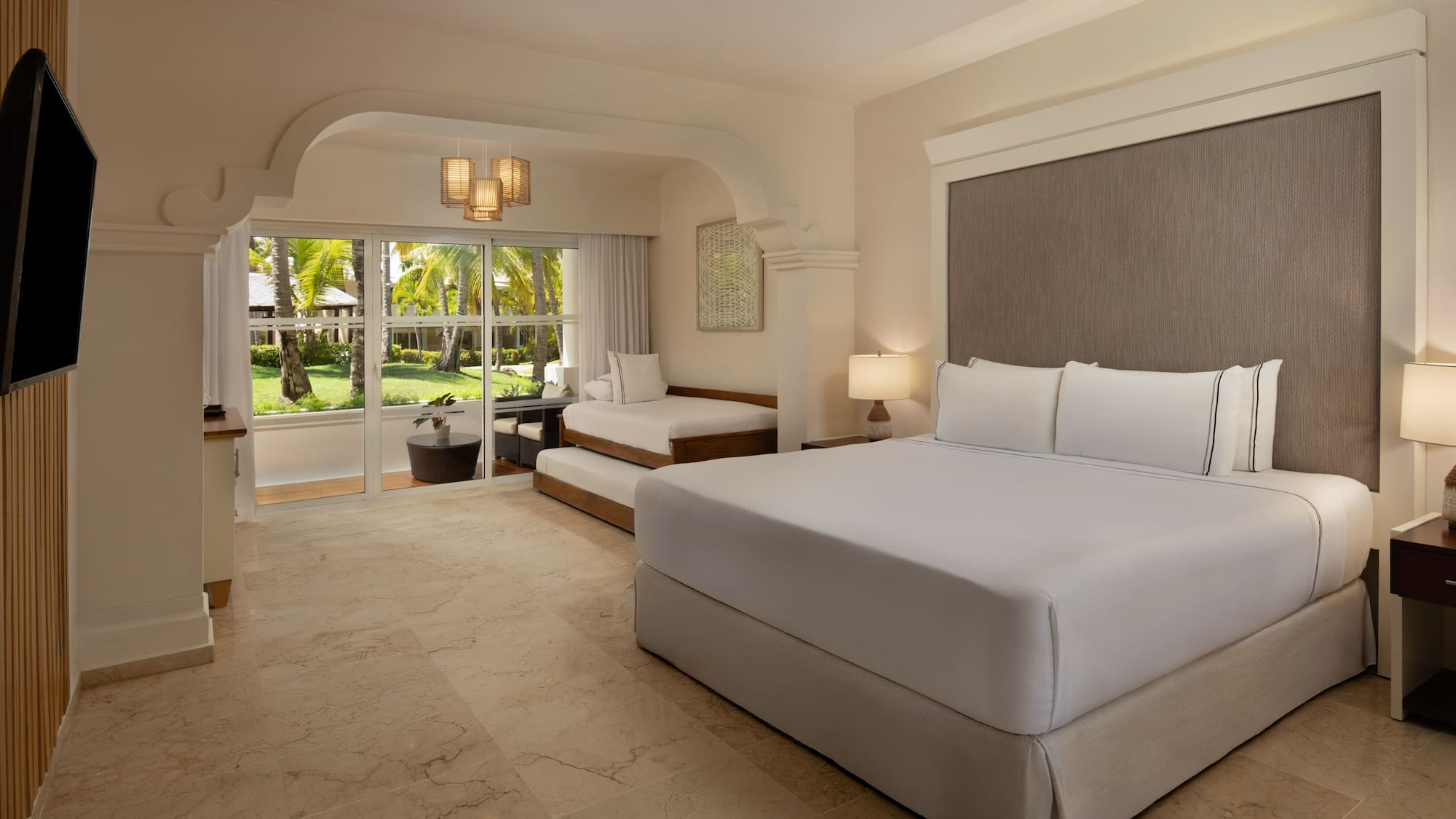 Resort room with king bed, daybed, and lush tropical garden view.