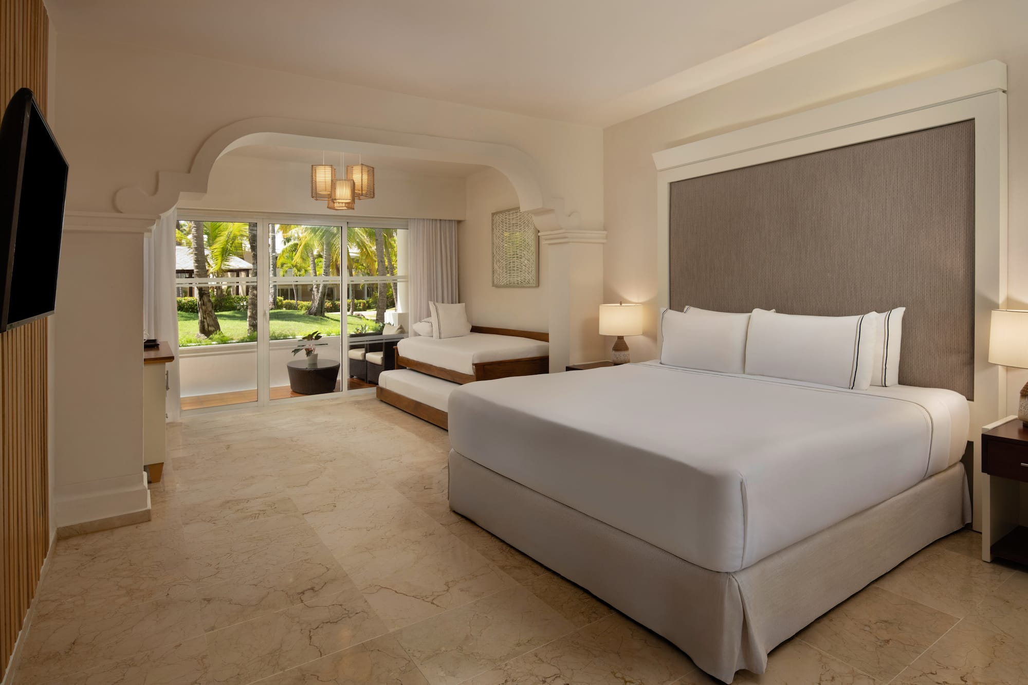 Resort room with king bed, daybed, and lush tropical garden view.