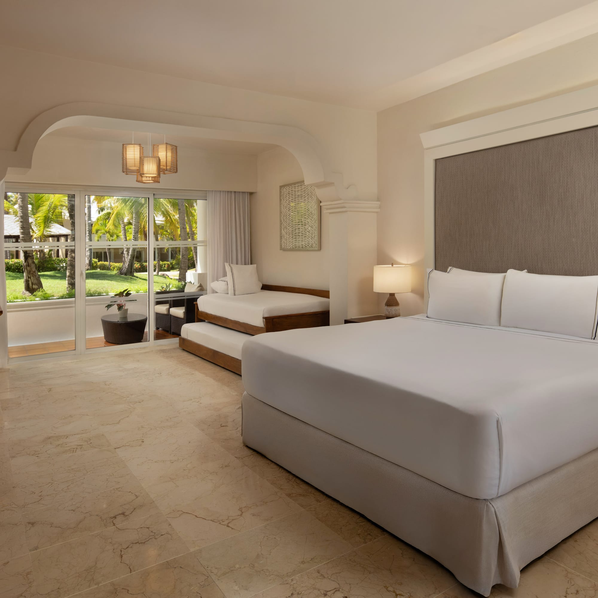 Resort room with king bed, daybed, and lush tropical garden view.