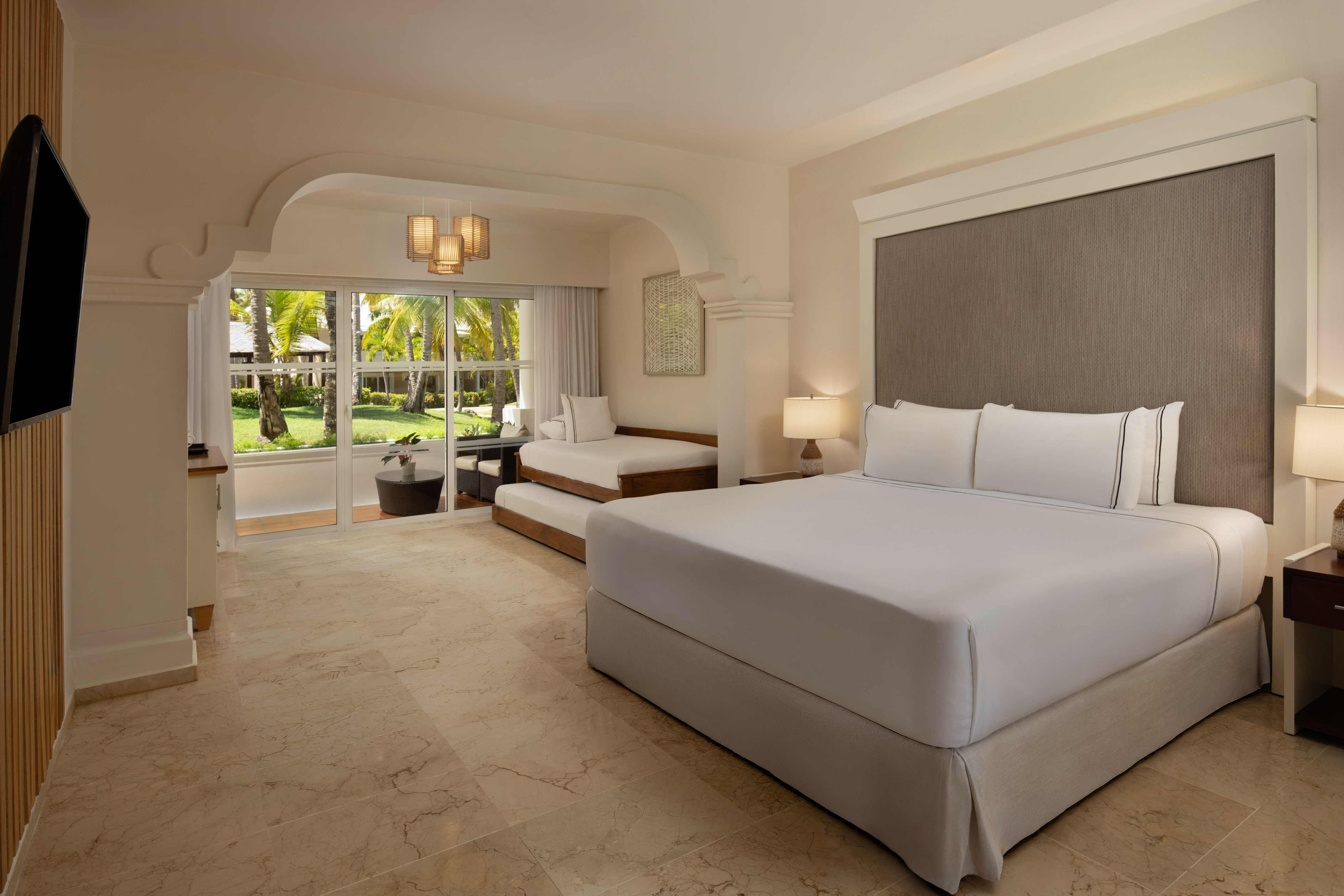 Resort room with king bed, daybed, and lush tropical garden view.