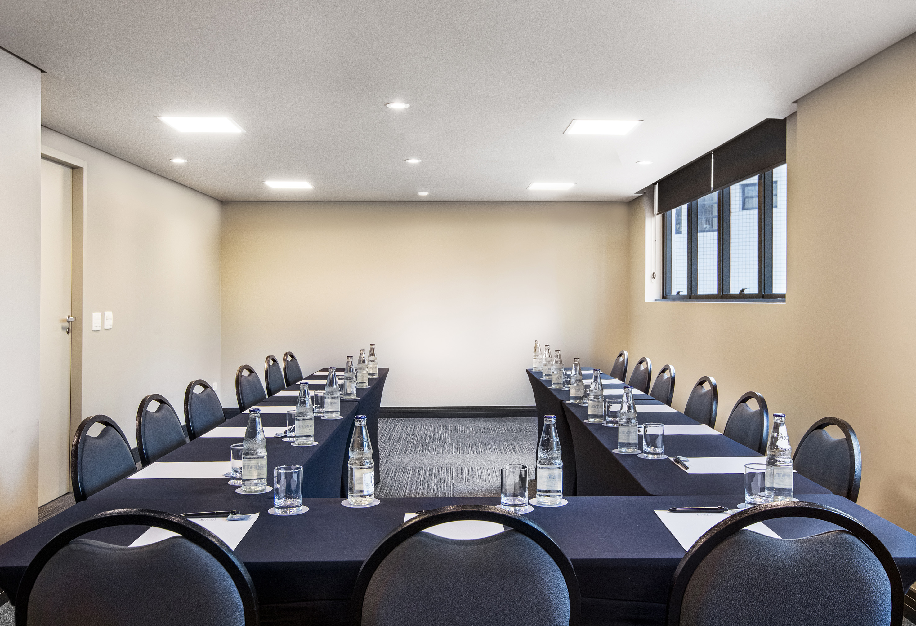 U-shaped conference room with dark tables, chairs, water bottles, and notepads.