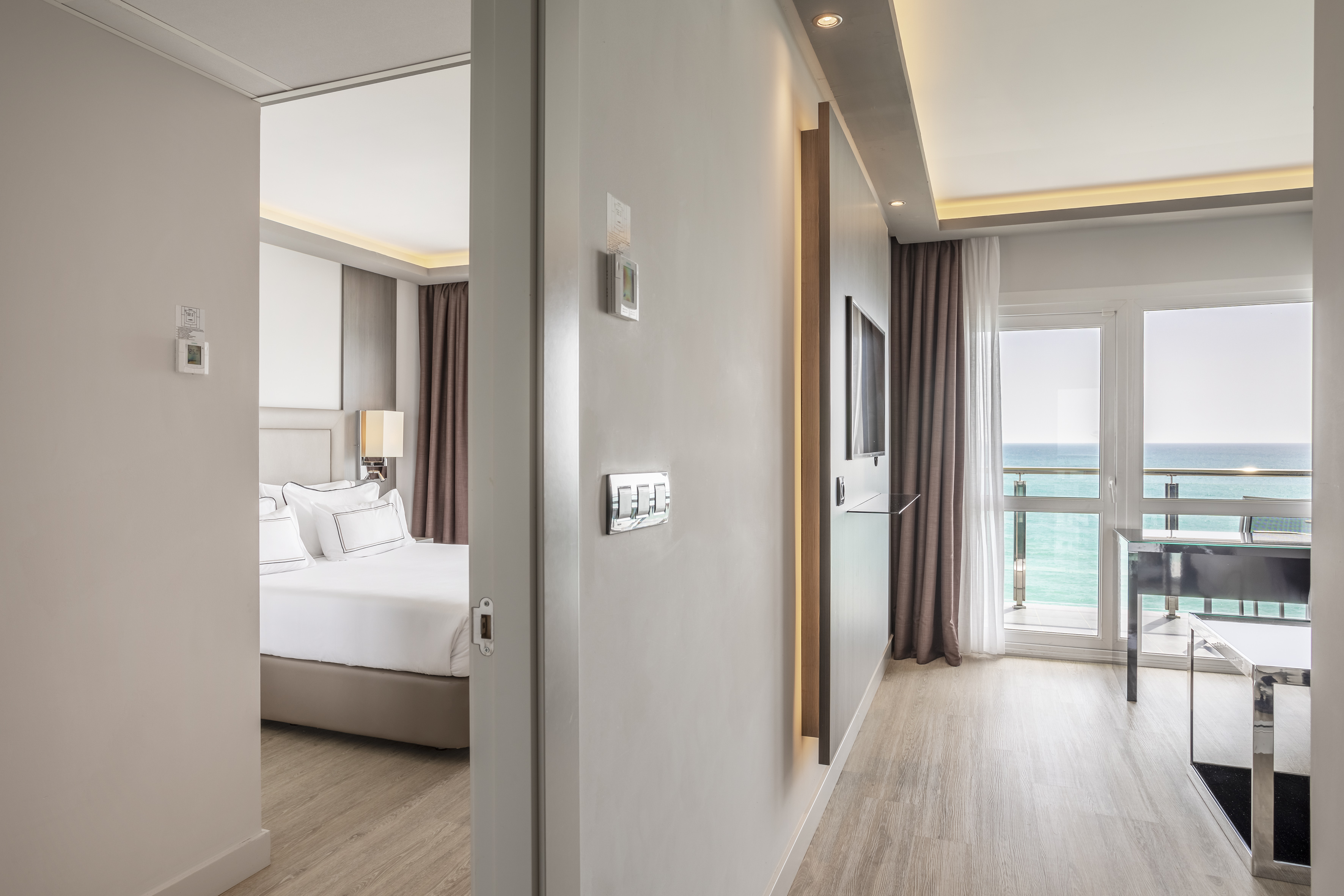 Modern hotel suite with bedroom, living area, and ocean view balcony.