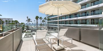 a deck with chairs and umbrella on a balcony with palm trees and a blue sky