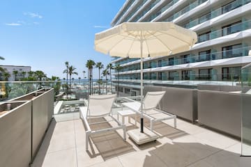 a deck with chairs and umbrella on a balcony with palm trees and a blue sky