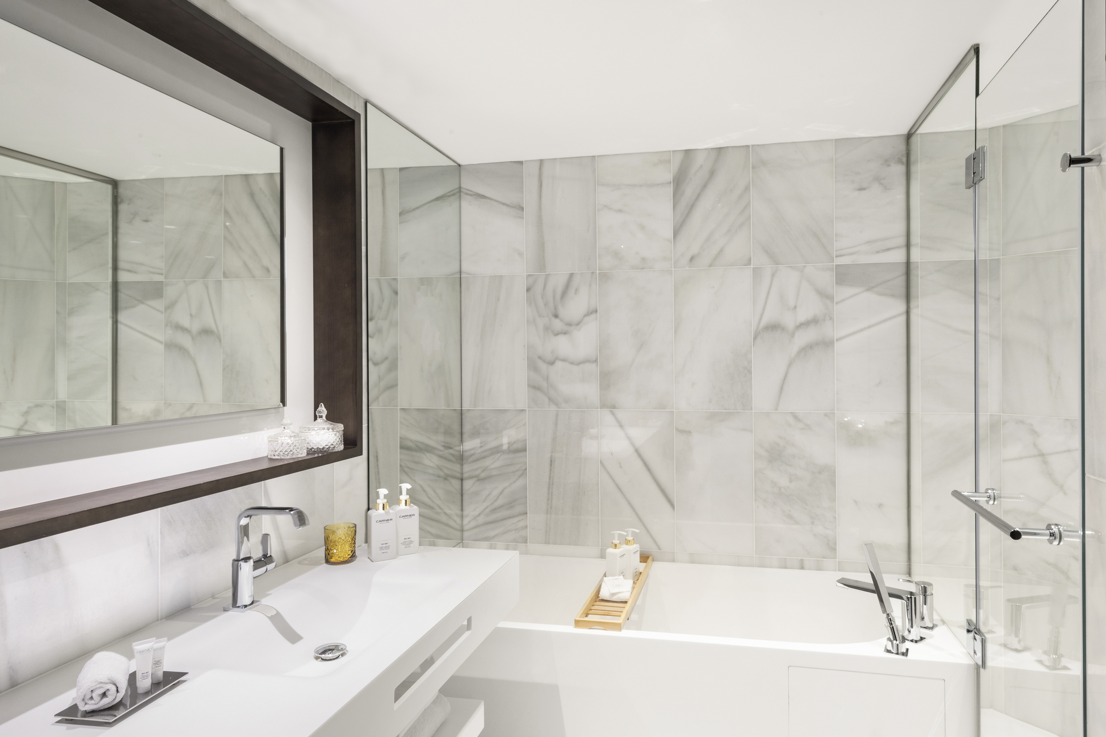 Modern luxury bathroom with white marble walls, sleek vanity, and bathtub.
