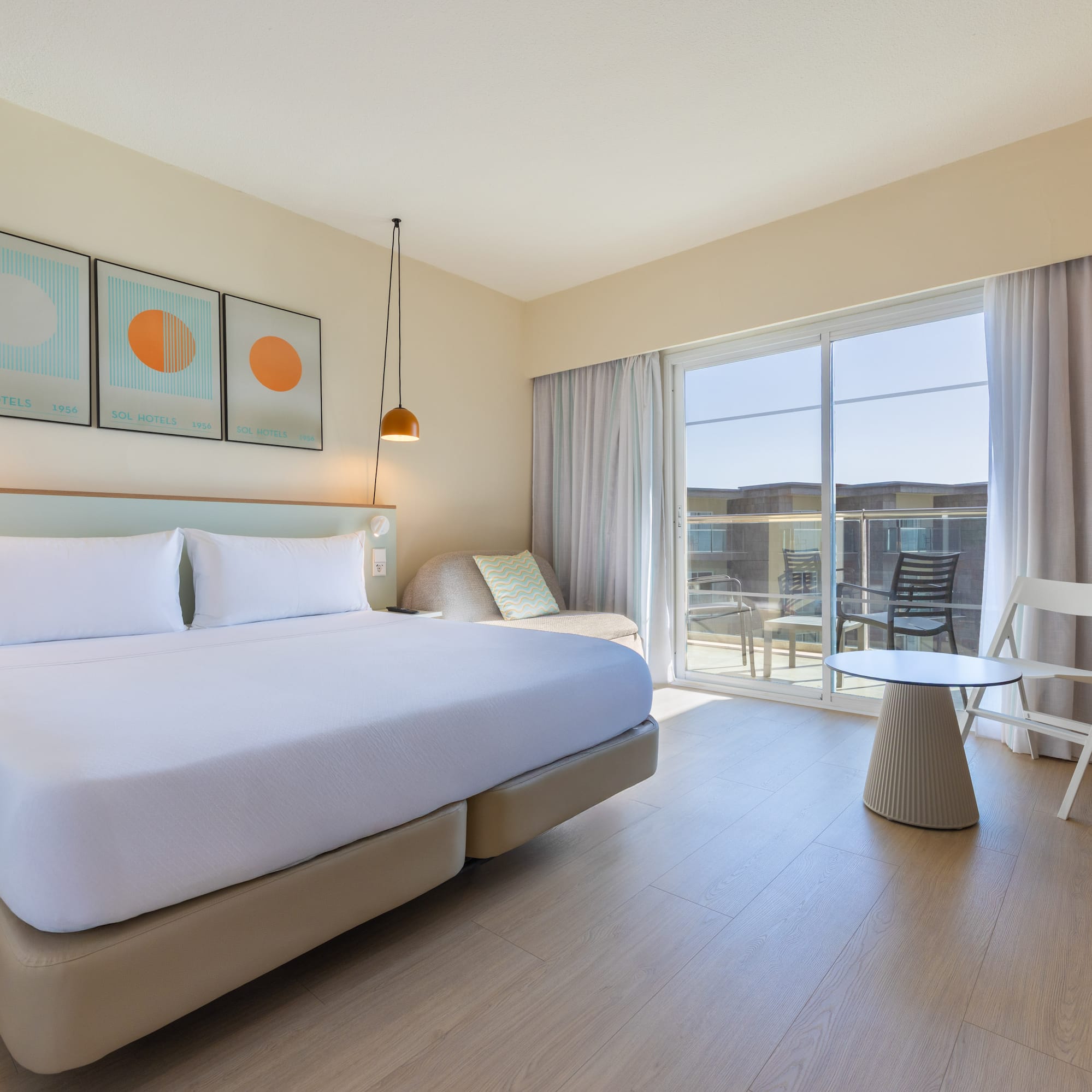 Bright hotel room with large bed, balcony, modern decor, and light wood floor.