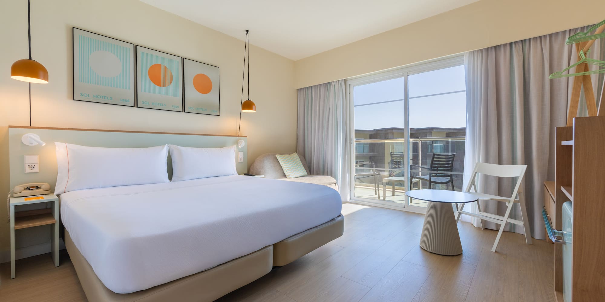 Bright hotel room with large bed, balcony, modern decor, and light wood floor.