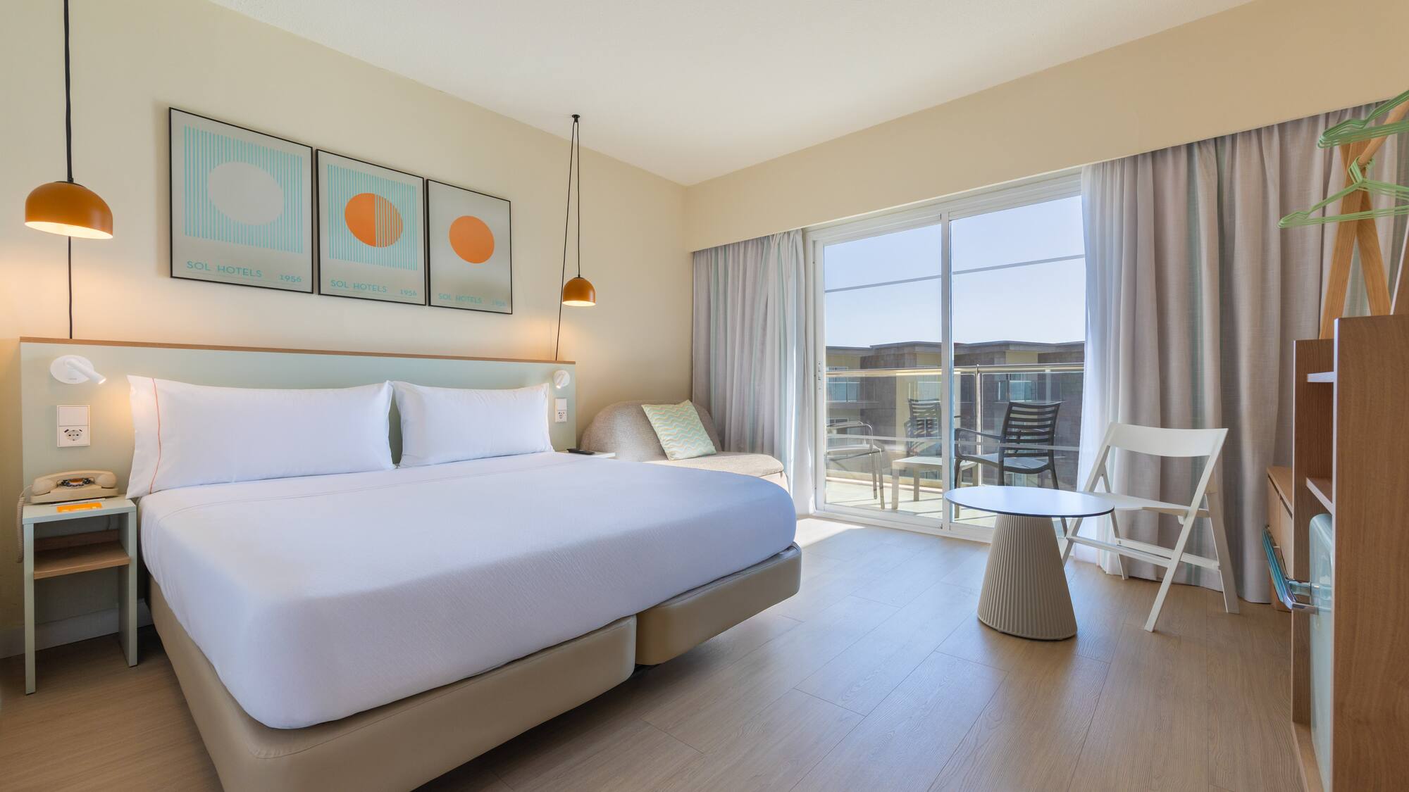 Bright hotel room with large bed, balcony, modern decor, and light wood floor.