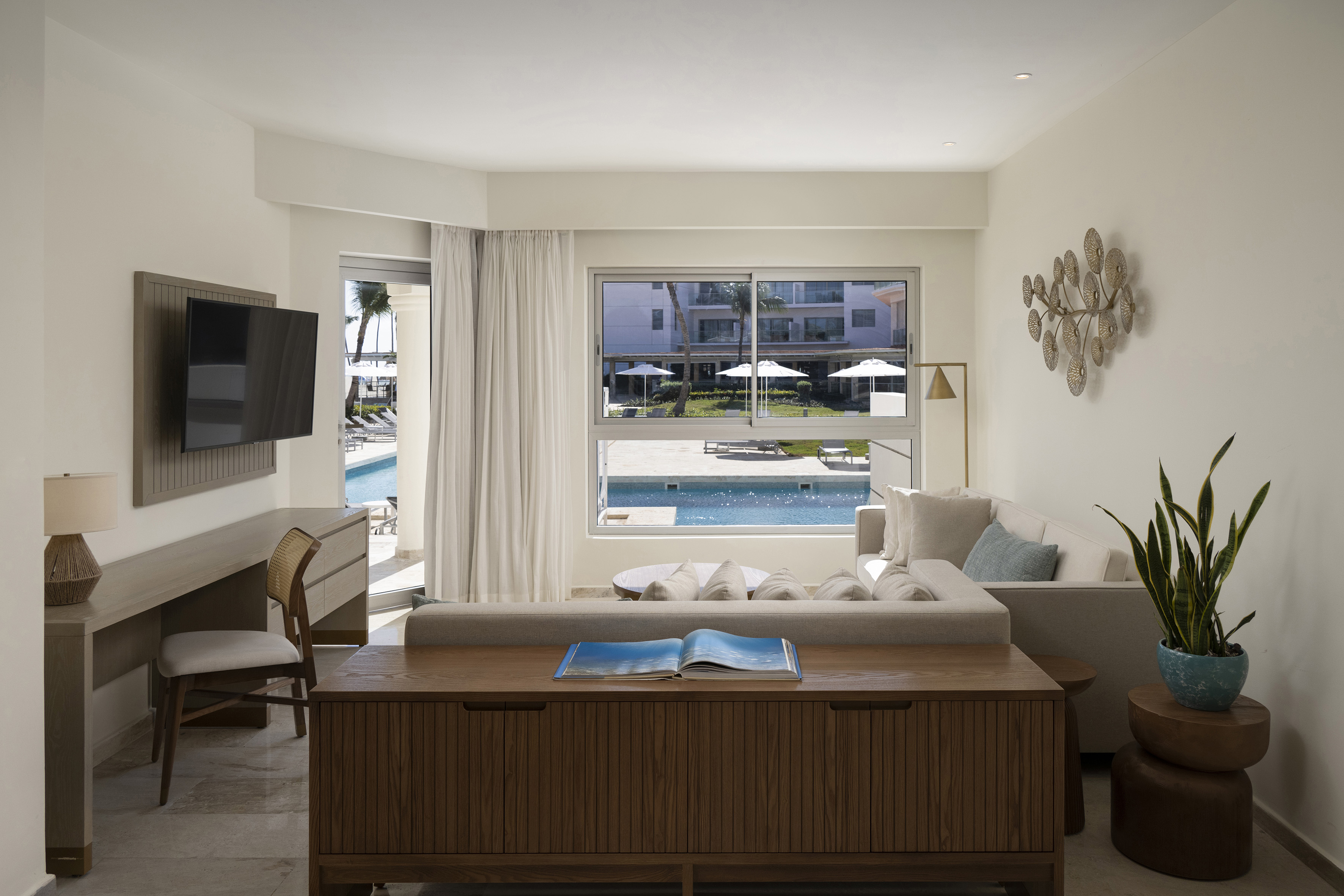 Modern resort suite living room with pool view, sofa, TV, and desk.