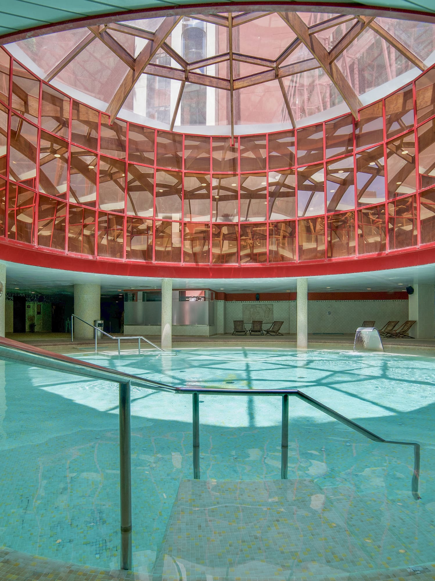 Round indoor pool with red-framed glass dome ceiling, spa water features.