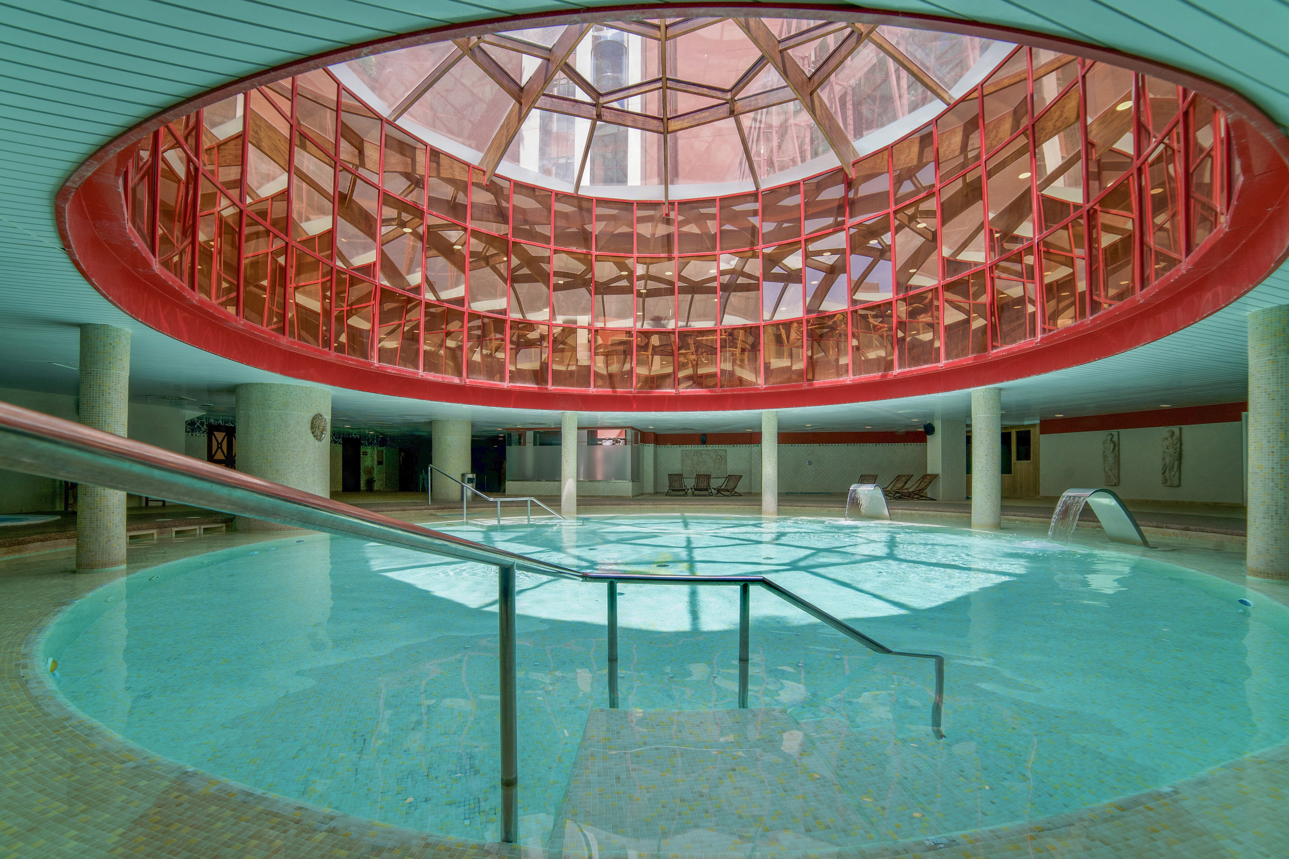 Round indoor pool with red-framed glass dome ceiling, spa water features.