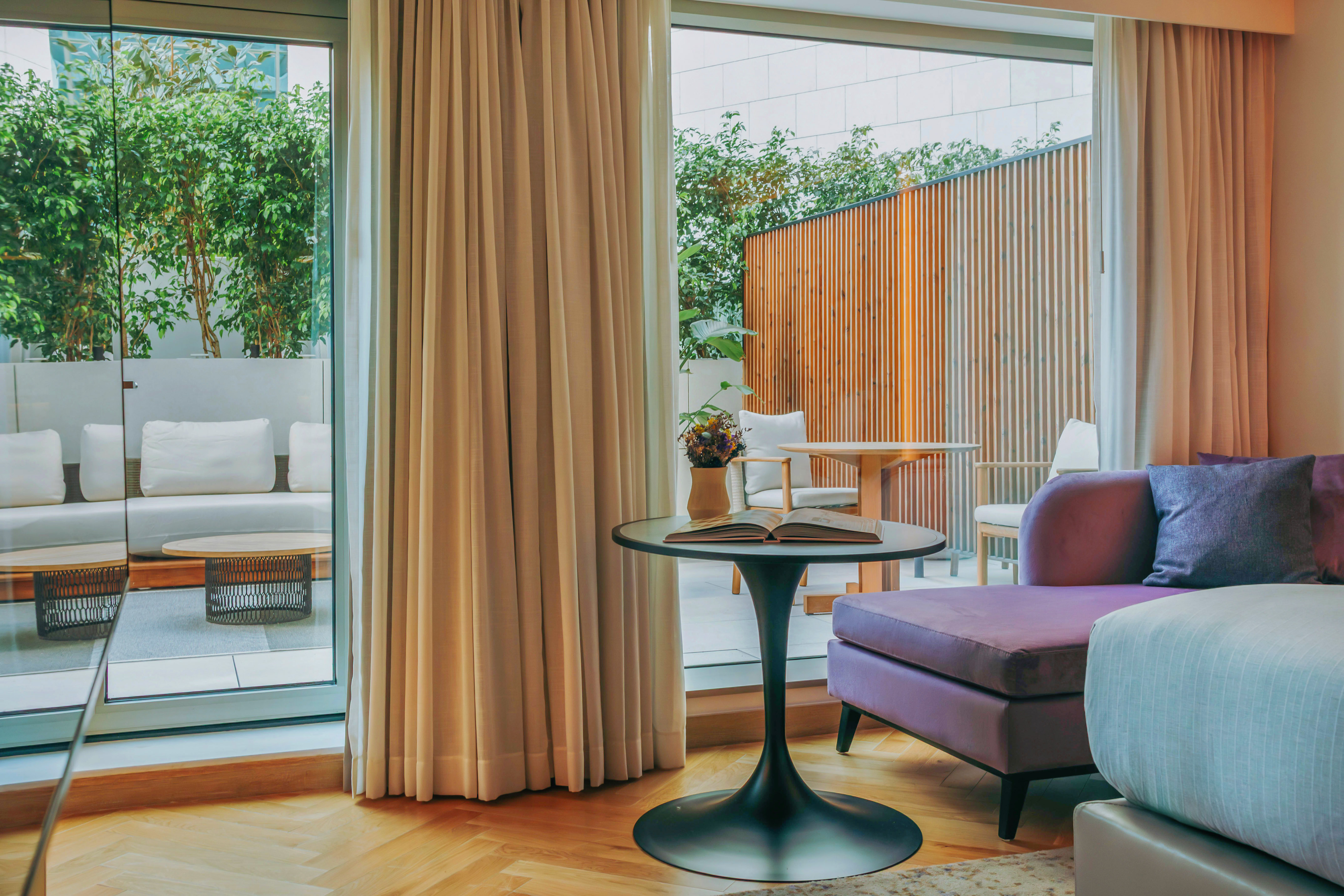 Modern hotel suite with purple sofa, outdoor patio, and lush green plants.