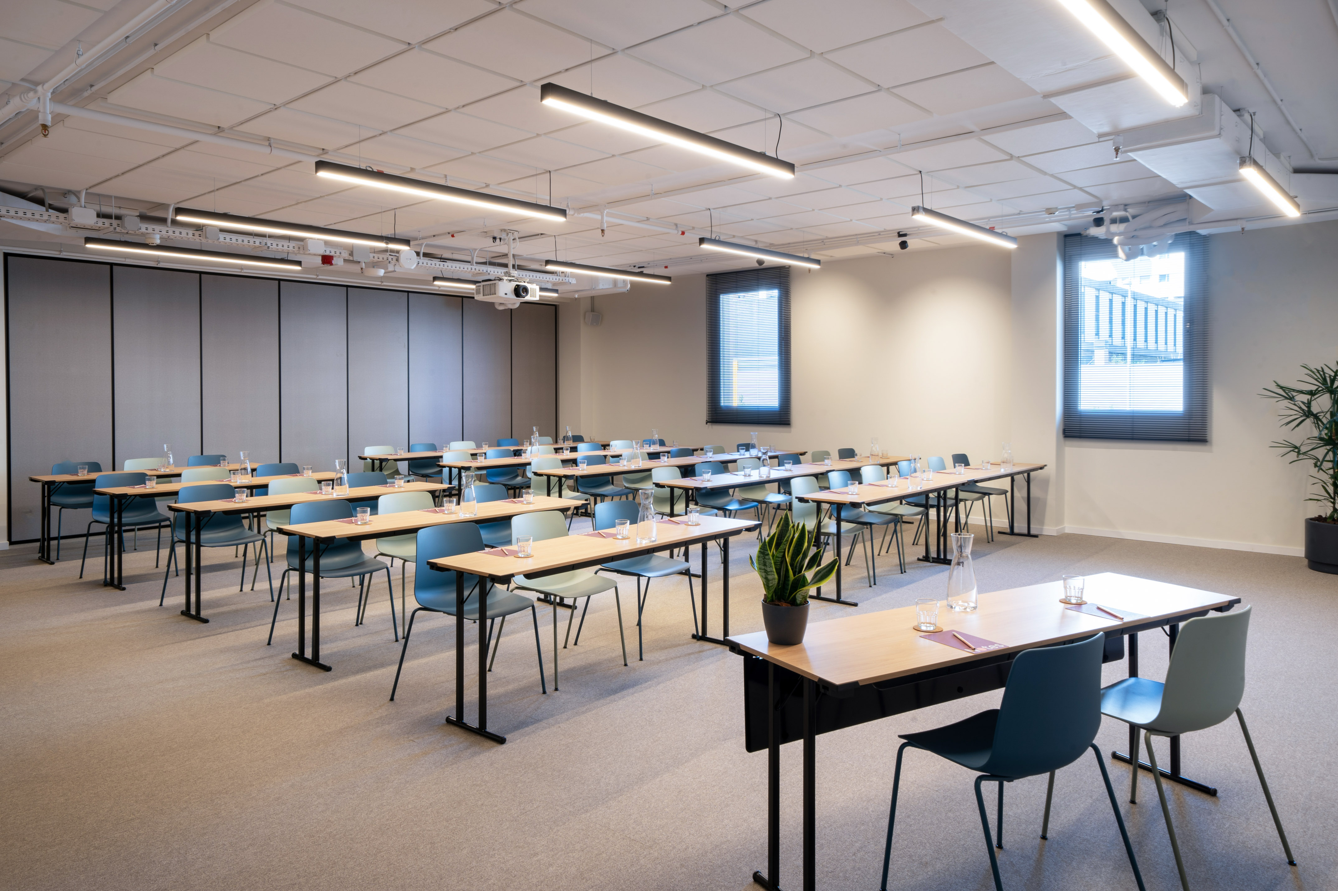 Modern training room with light wood tables, blue and green chairs, projector.