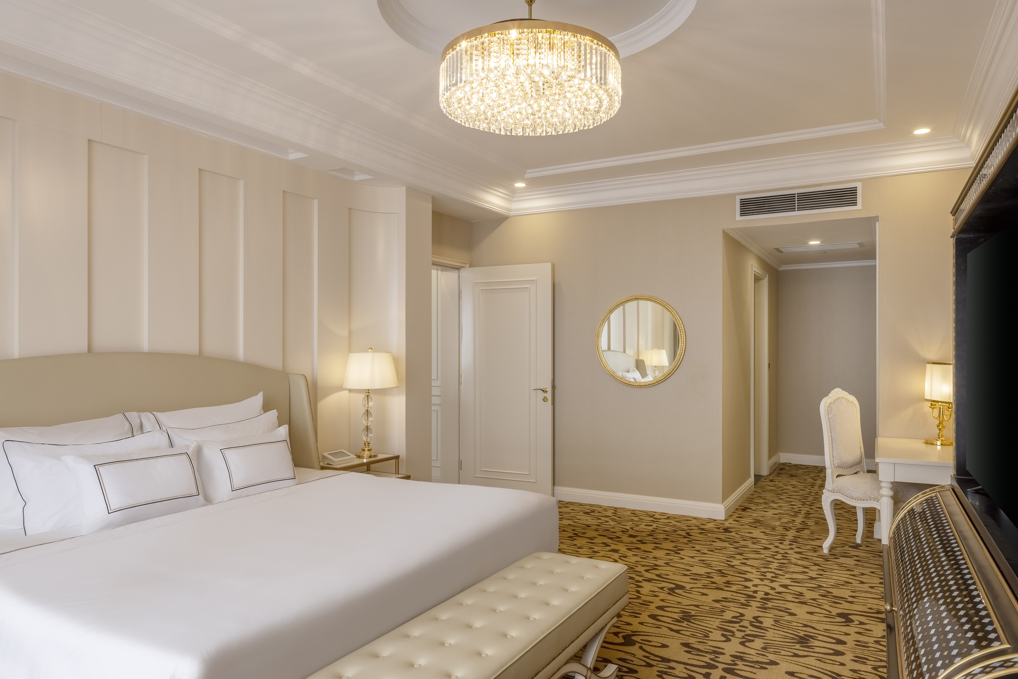 Hotel bedroom with king bed, crystal chandelier, and classic luxury decor.