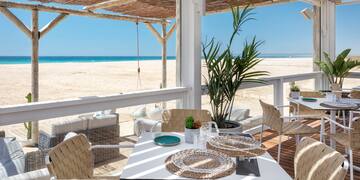 a table and chairs on a deck with a beach view