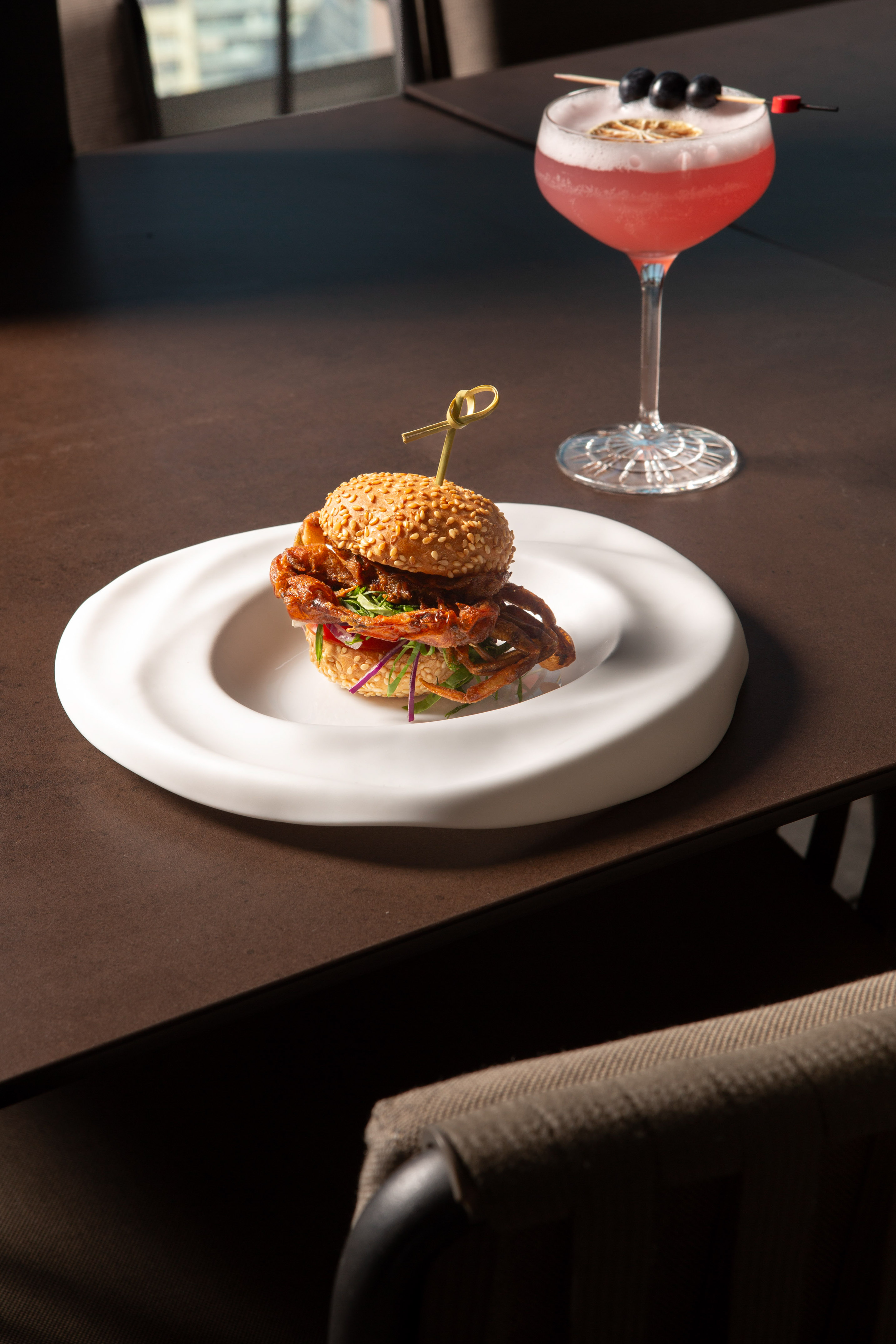 Soft-shell crab slider, sesame bun, and pink cocktail in a restaurant.