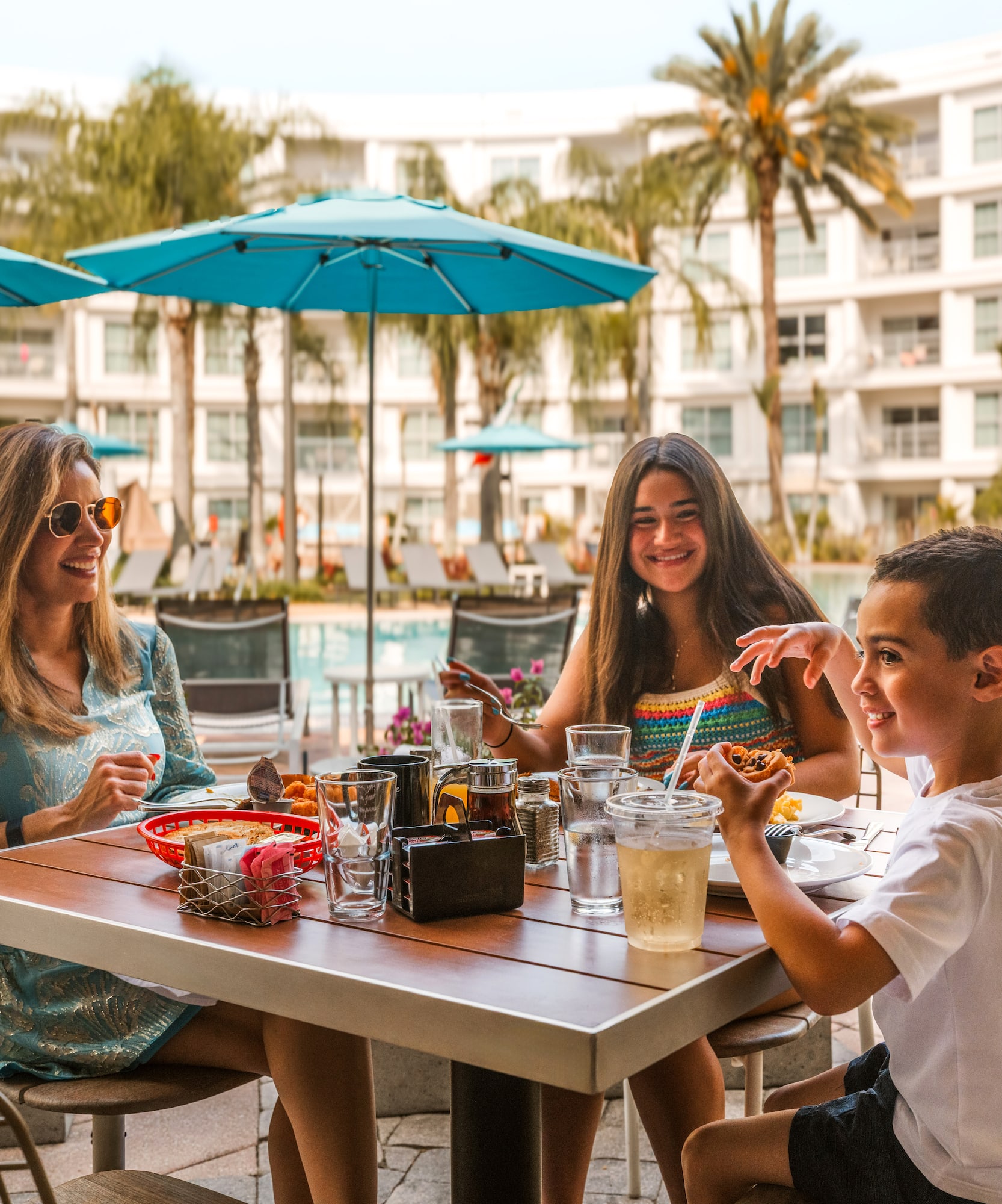 Family dining poolside at a vibrant resort restaurant with palm trees.