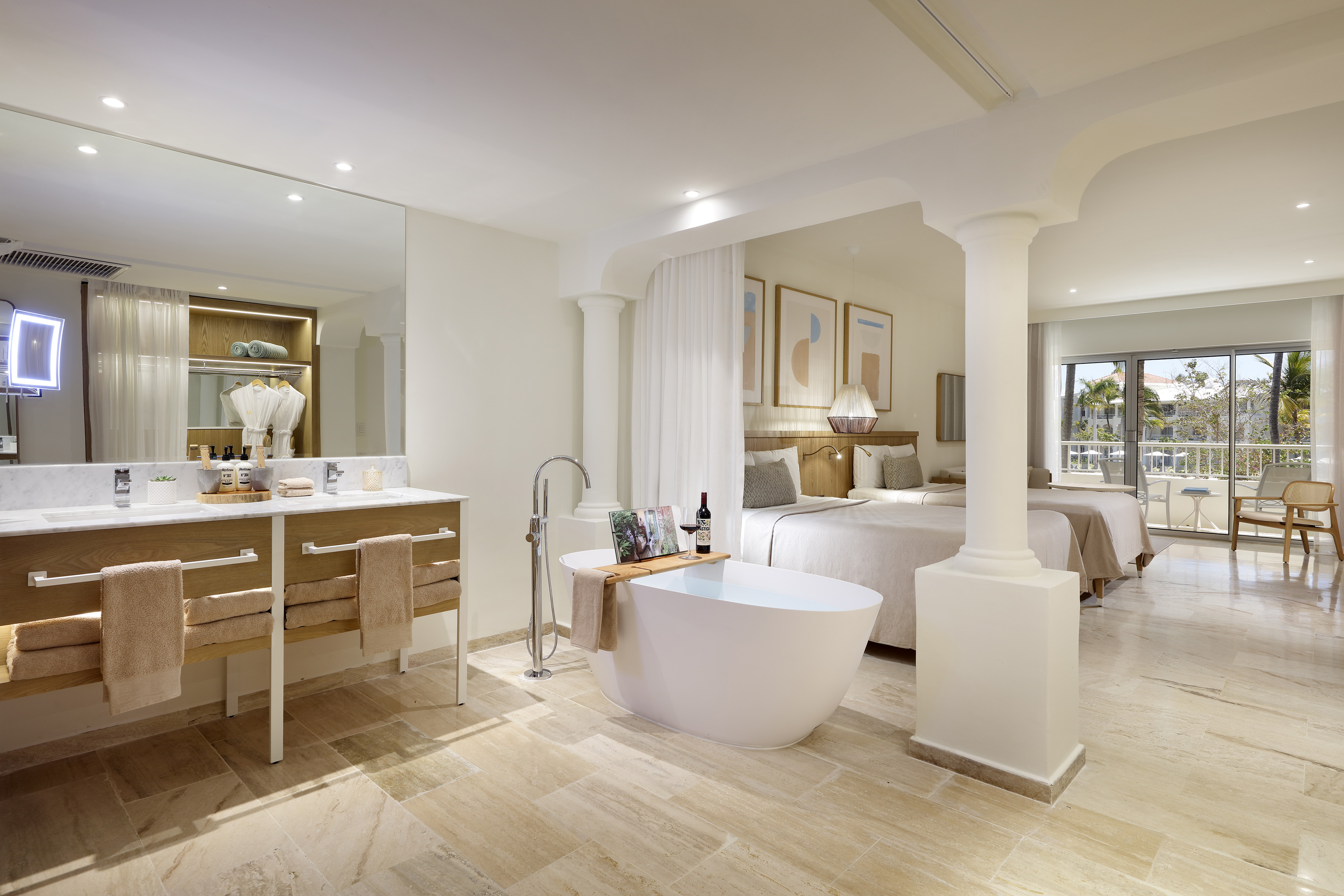 Hotel suite: freestanding tub, two beds, double vanity, private balcony.