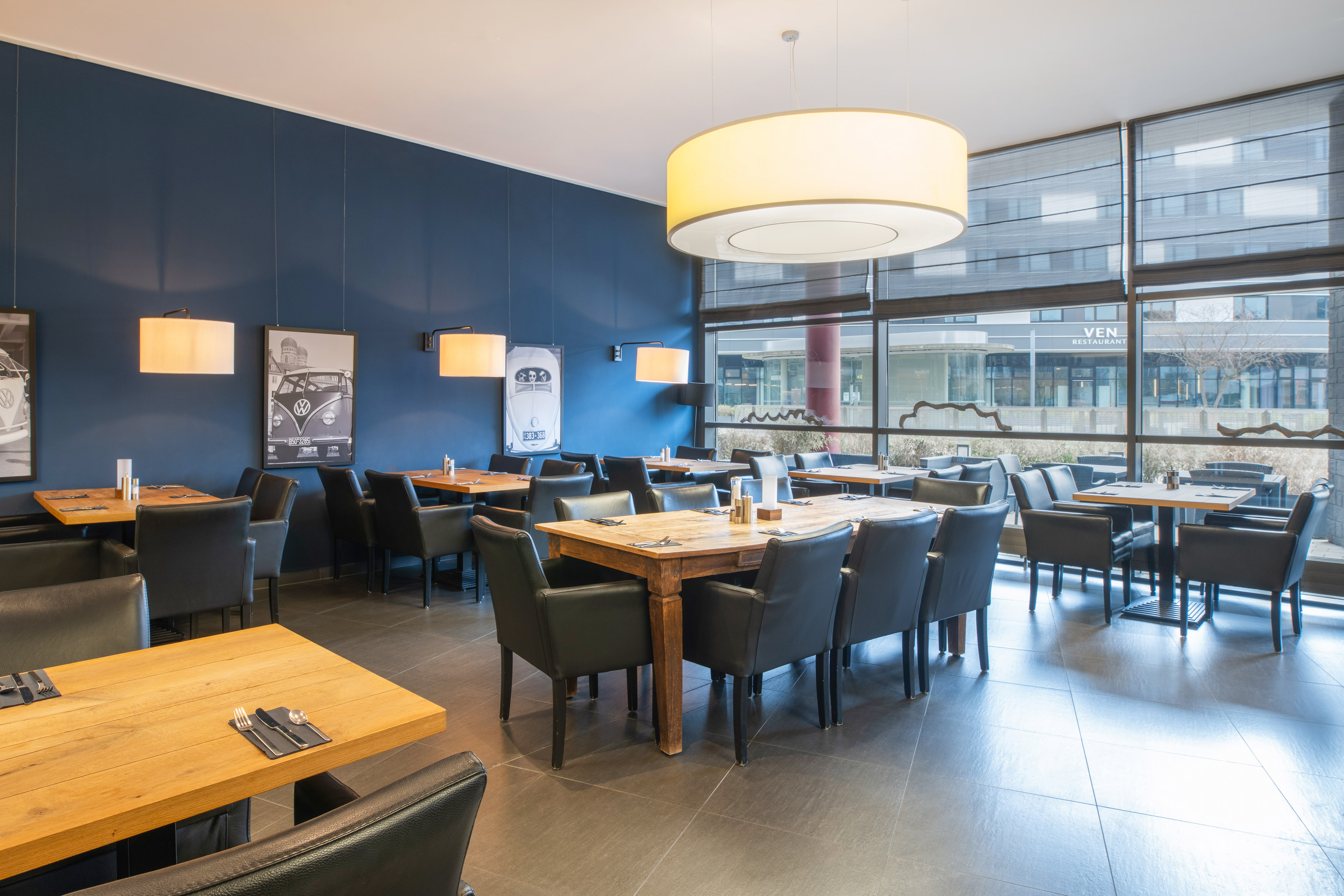 Modern restaurant interior: blue wall, wooden tables, black chairs, VW bus posters.
