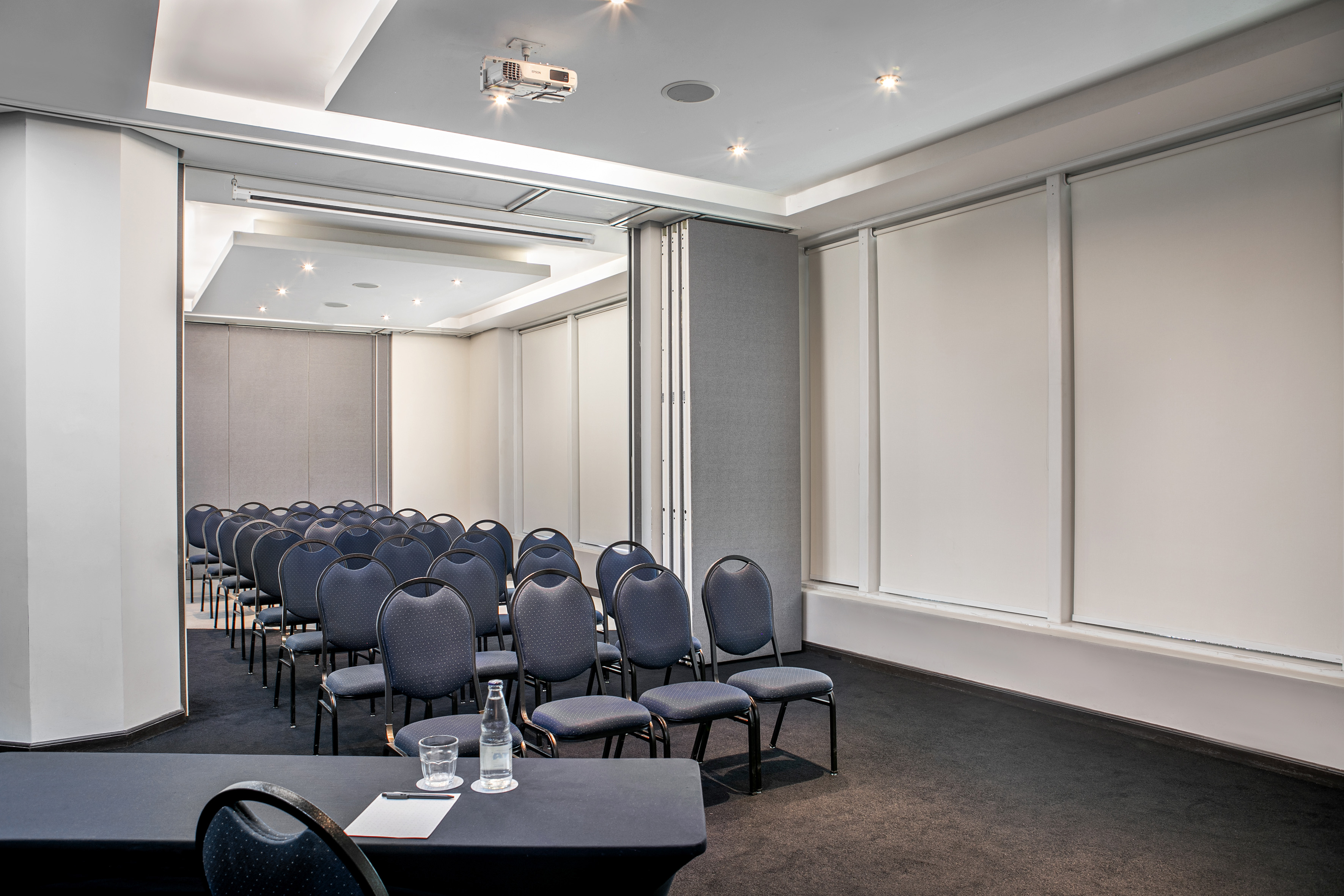 Modern conference room with blue chairs, ceiling projector, and partition walls.