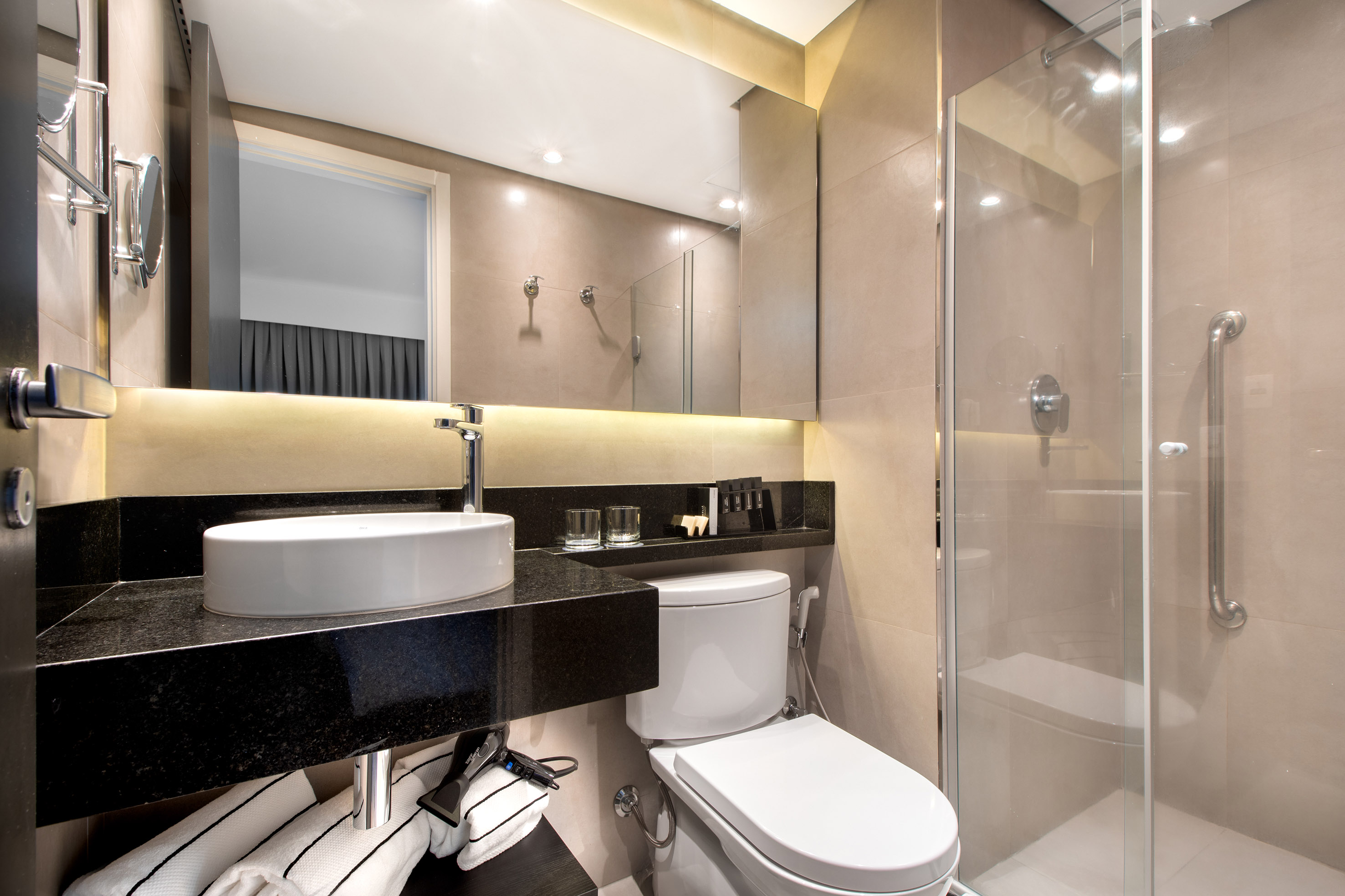 Modern hotel bathroom with vessel sink, black granite vanity, toilet, and glass shower.