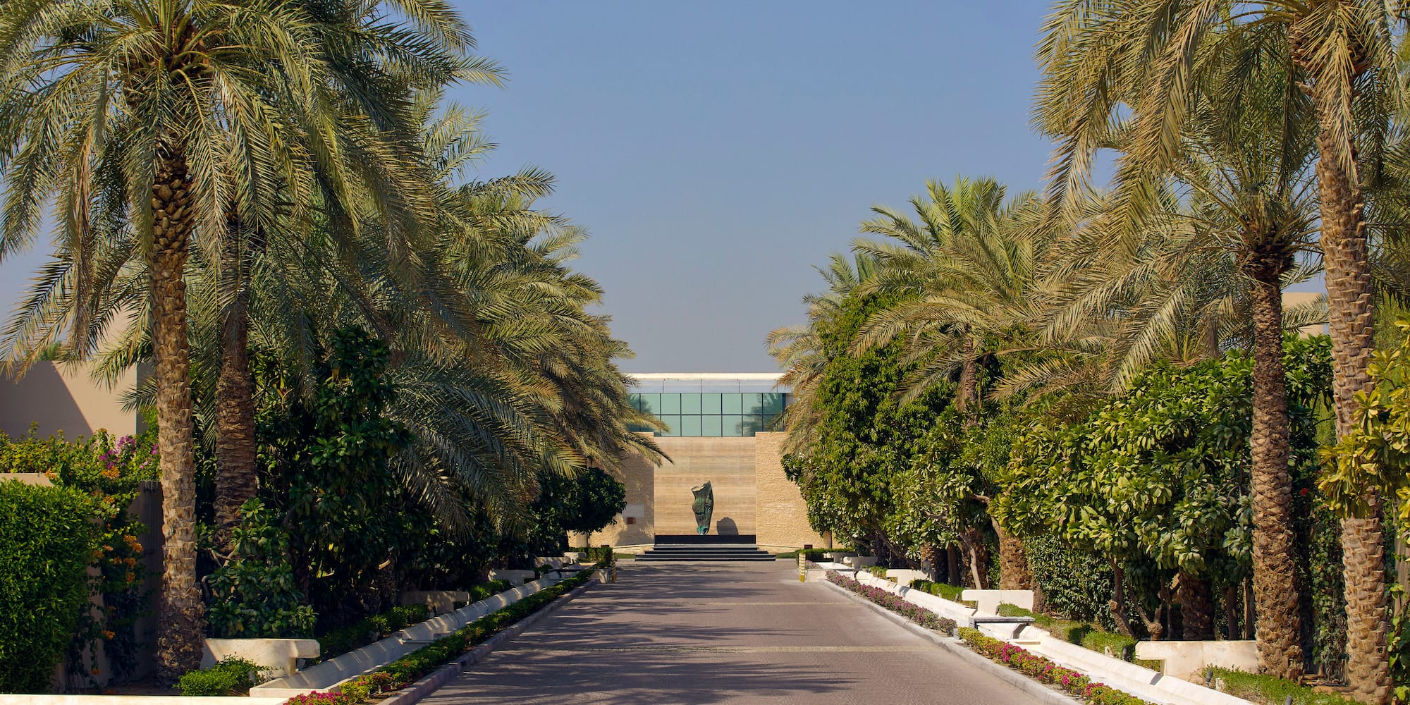 a road with palm trees and a statue on the side