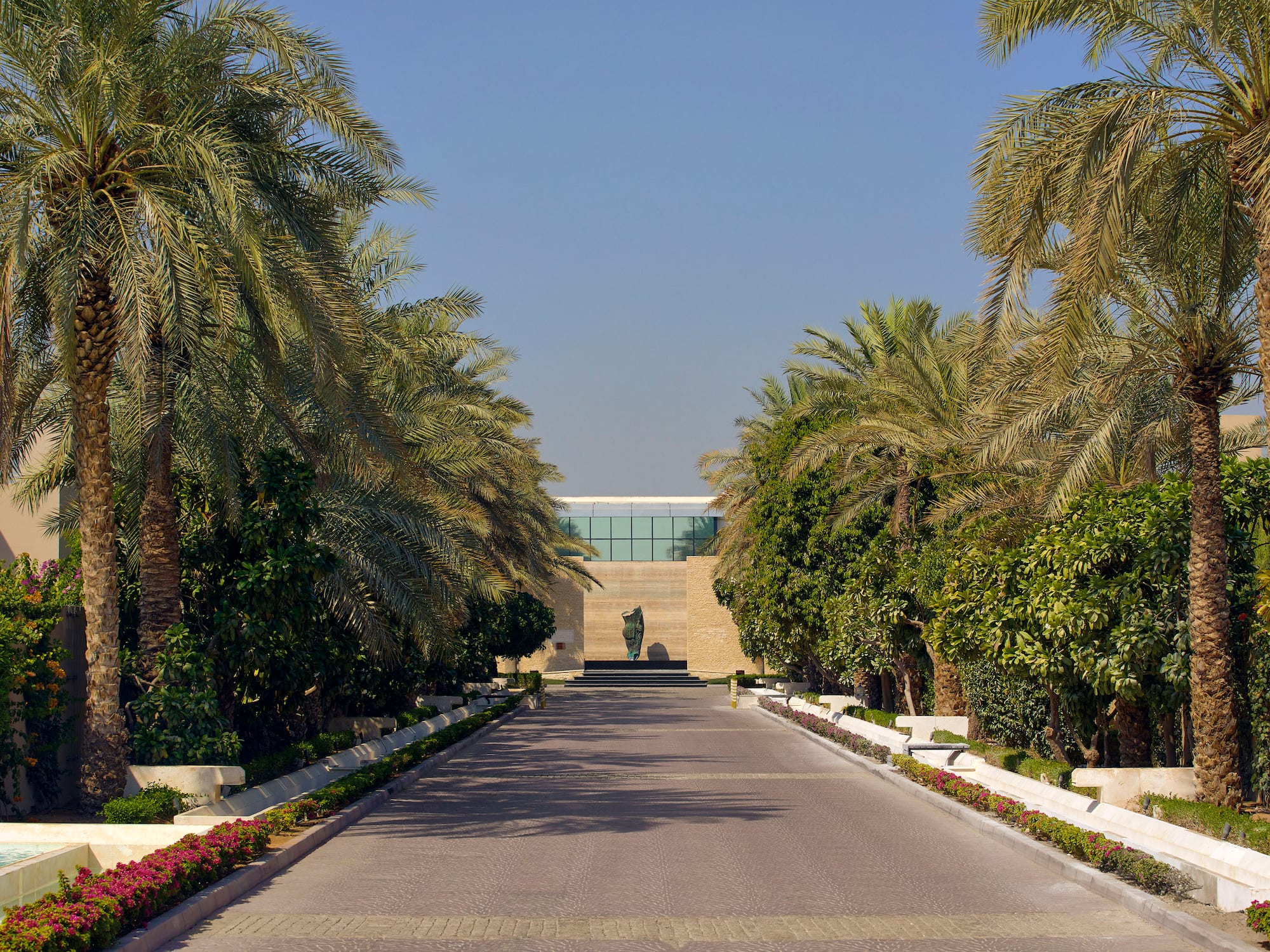 a road with palm trees and a statue on the side
