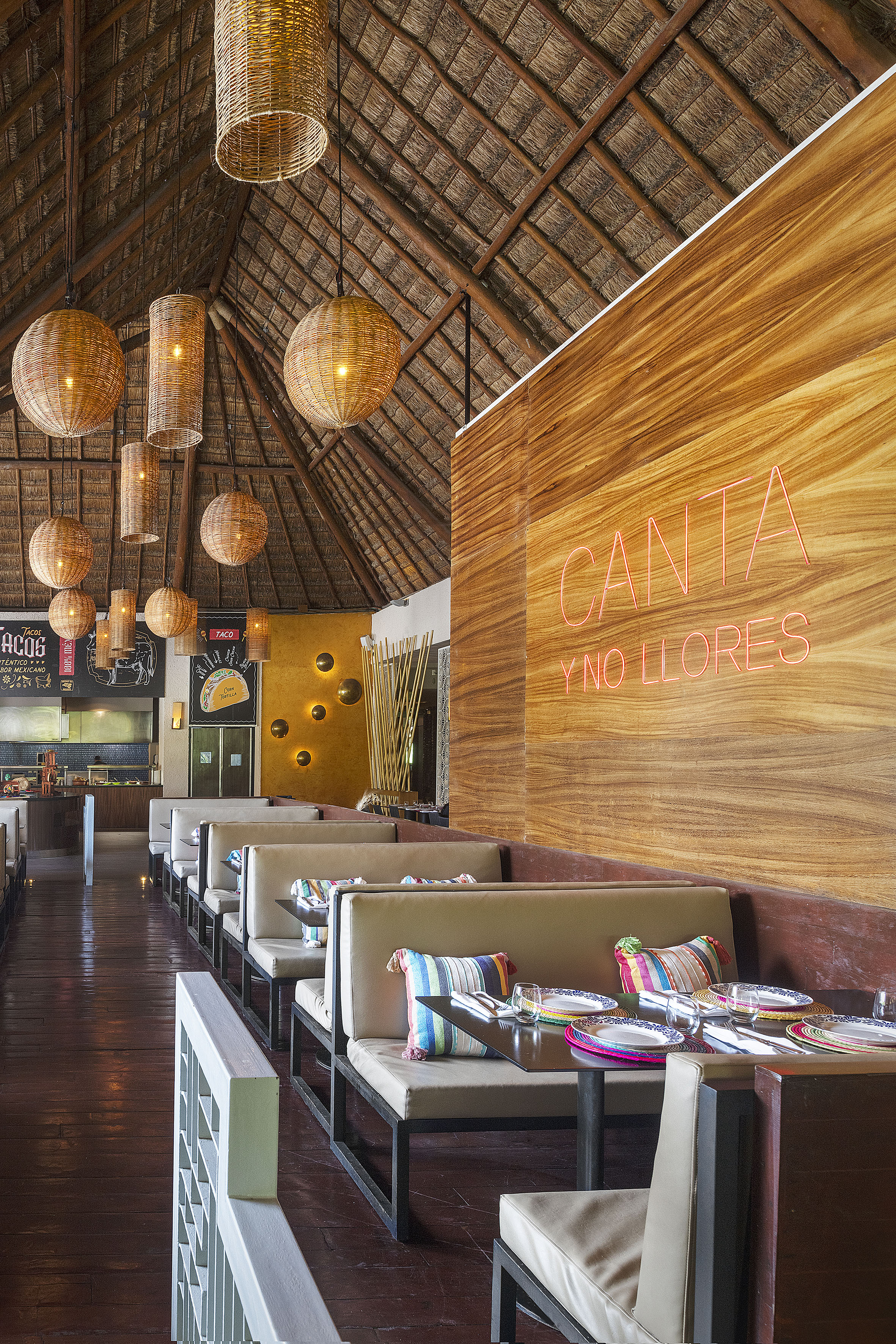 Tropical restaurant with thatched roof, rattan lights, and vibrant decor.