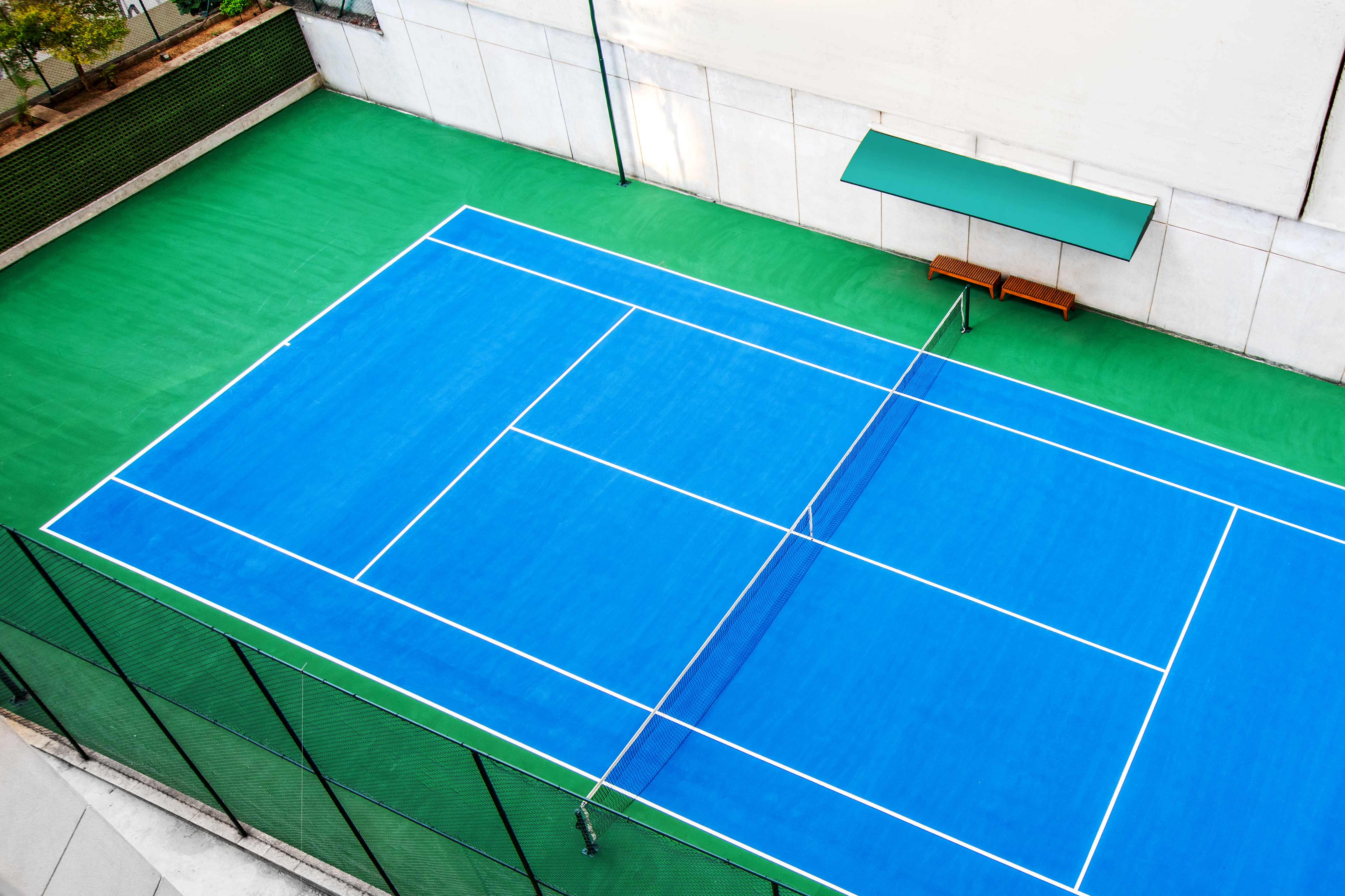 Vibrant blue tennis court with white lines, green surrounds, and net.